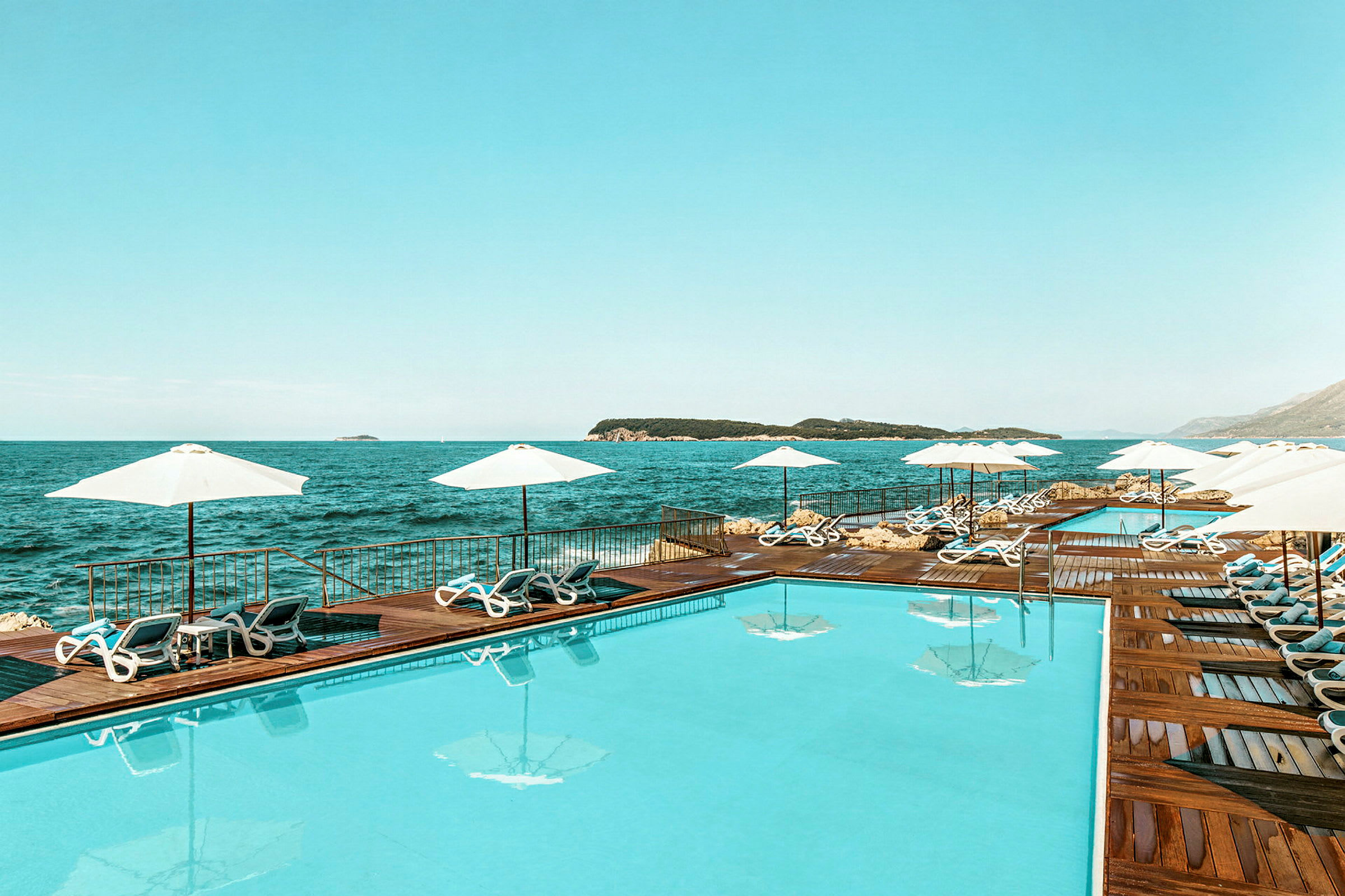 En swimmingpool vid havet, omgivet av solstolar och parasoller. (AI-genererad text)