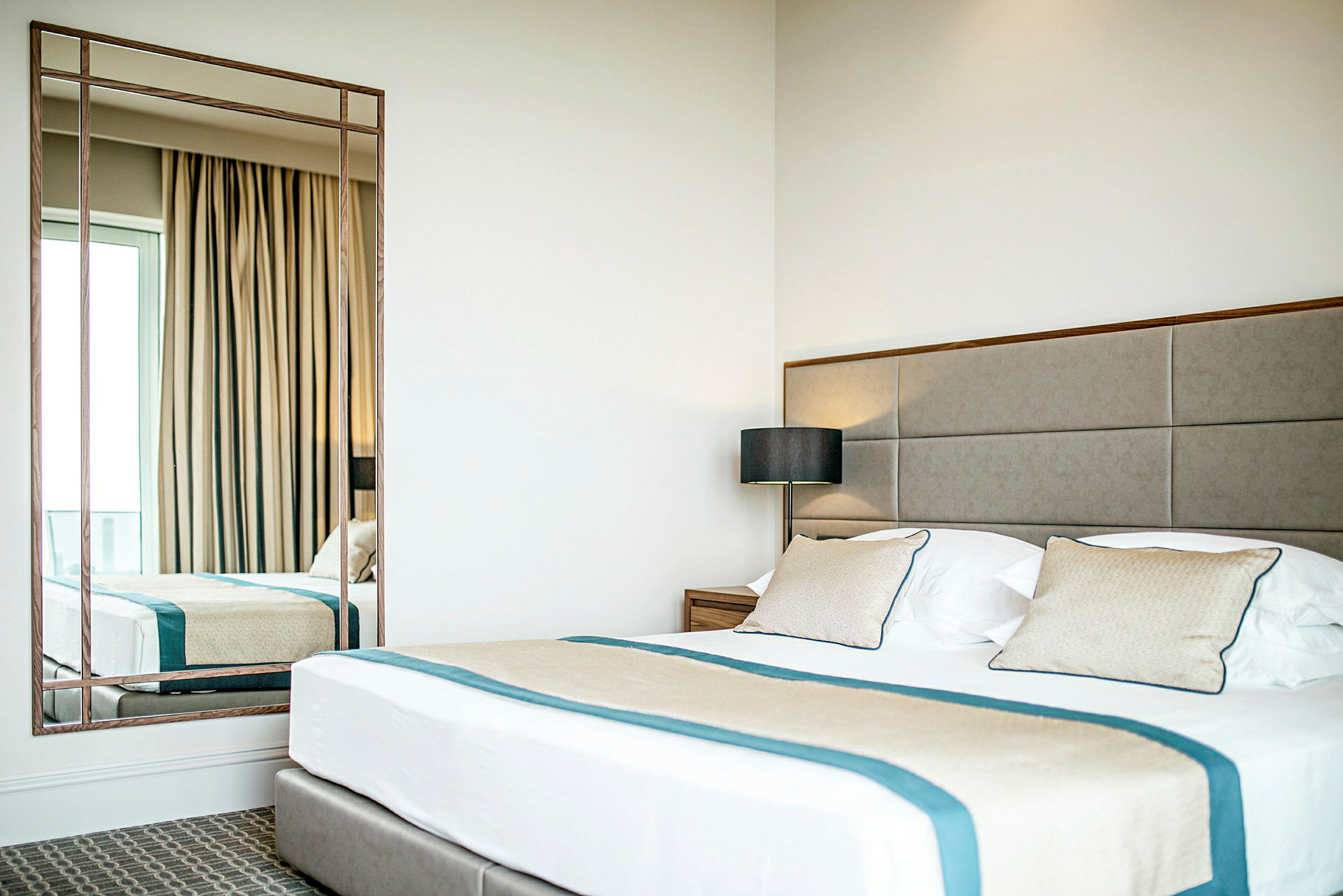 Ett hotellrum med en stor säng, kuddar och en spegel. (AI-genererad text)