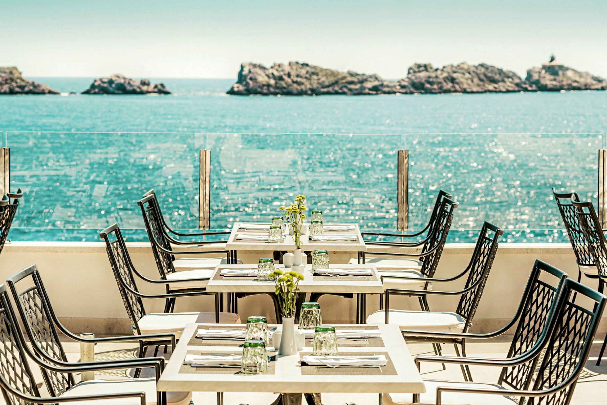En restaurangterrass med havsutsikt, bord och stolar står uppställda med dukning. (AI-genererad text)