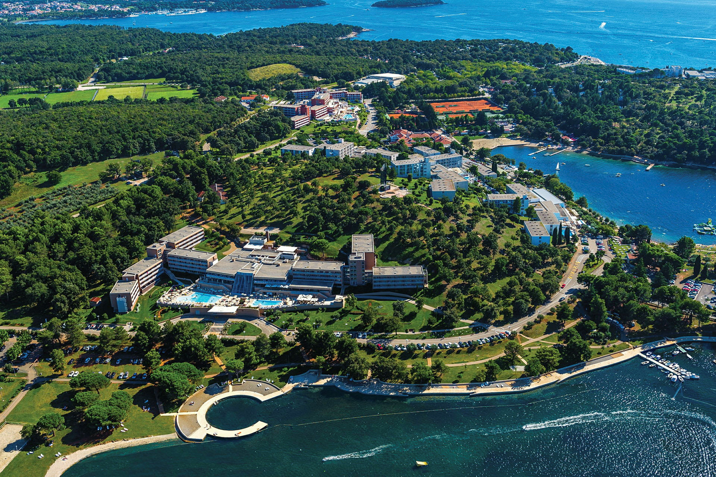 Flygfoto över en semesteranläggning vid kusten med gröna omgivningar och vy över havet. (AI-genererad text)