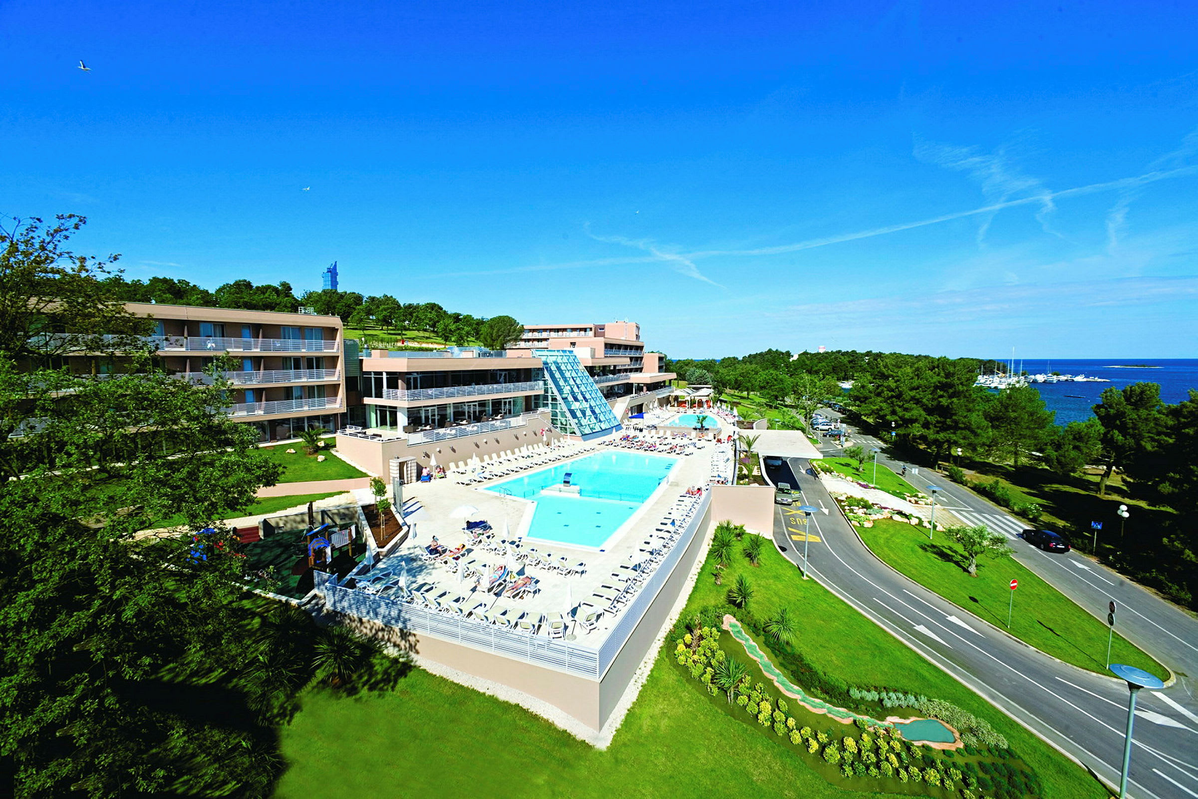 Bild på ett hotellkomplex med en pool och gröna omgivningar nära havet. (AI-genererad text)