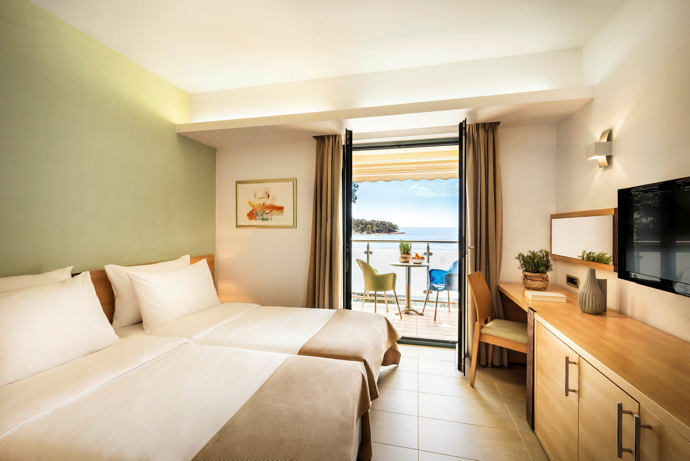 Ett hotellrum med två enkelsängar, en balkong med havsutsikt och en sittgrupp. (AI-genererad text)
