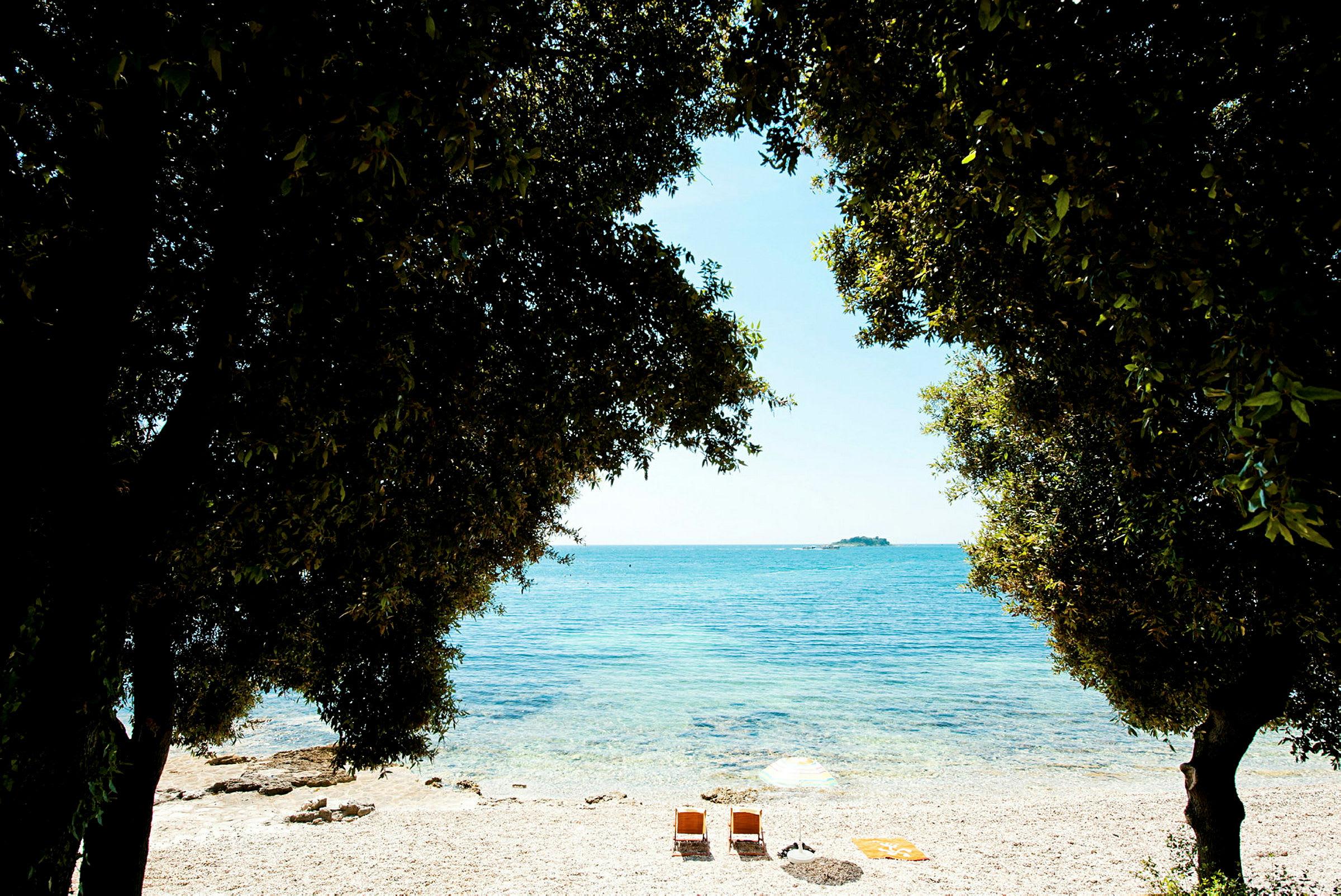 Bild av en stilla strand kantad av träd, med två solstolar och ett parasoll vid vattnet. (AI-genererad text)