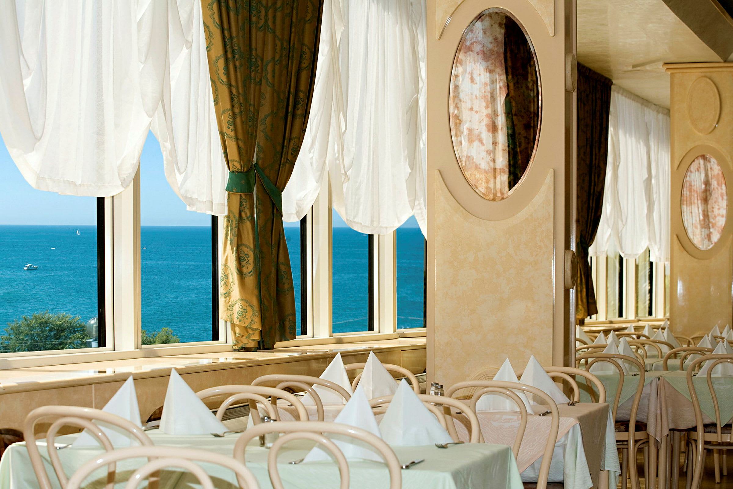 Restaurang med dukade bord vid fönster med utsikt över havet. (AI-genererad text)