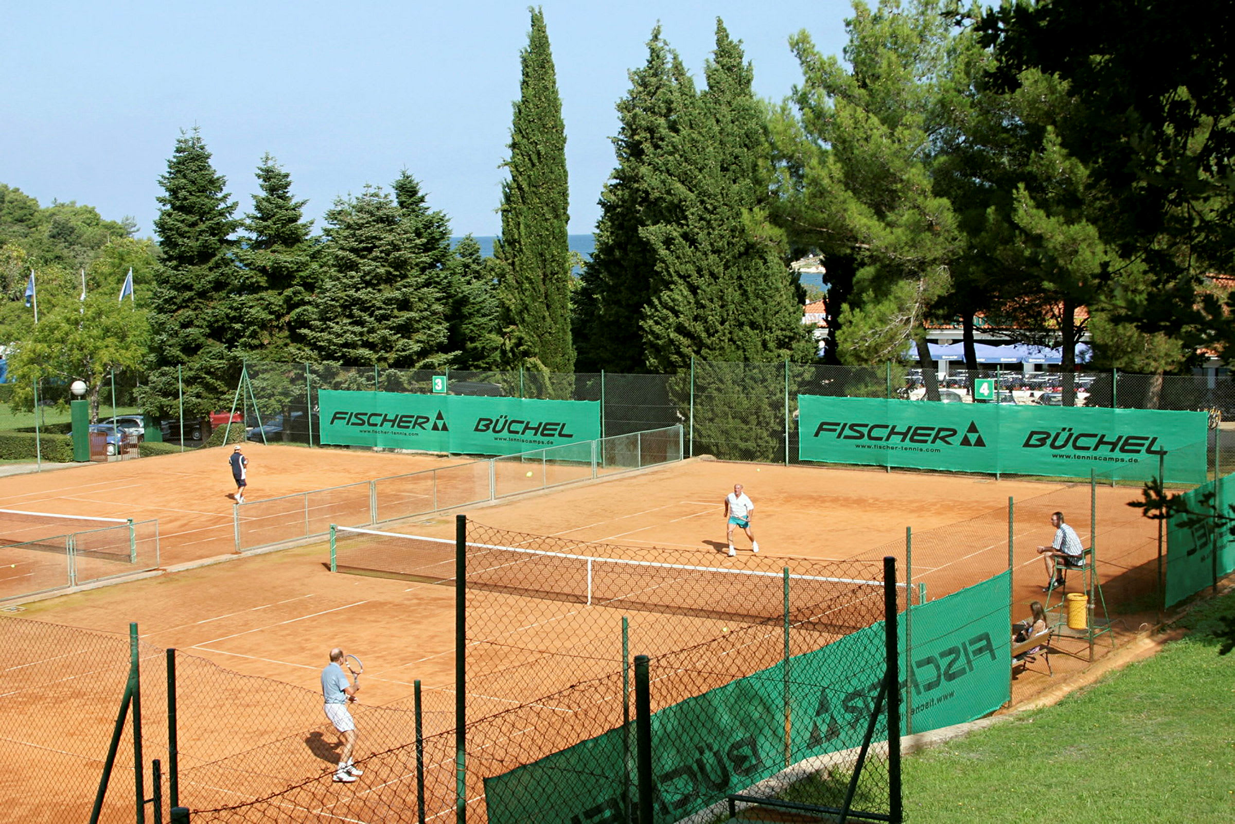 Tennisbanor med några spelare omgivna av träd och grönt. (AI-genererad text)