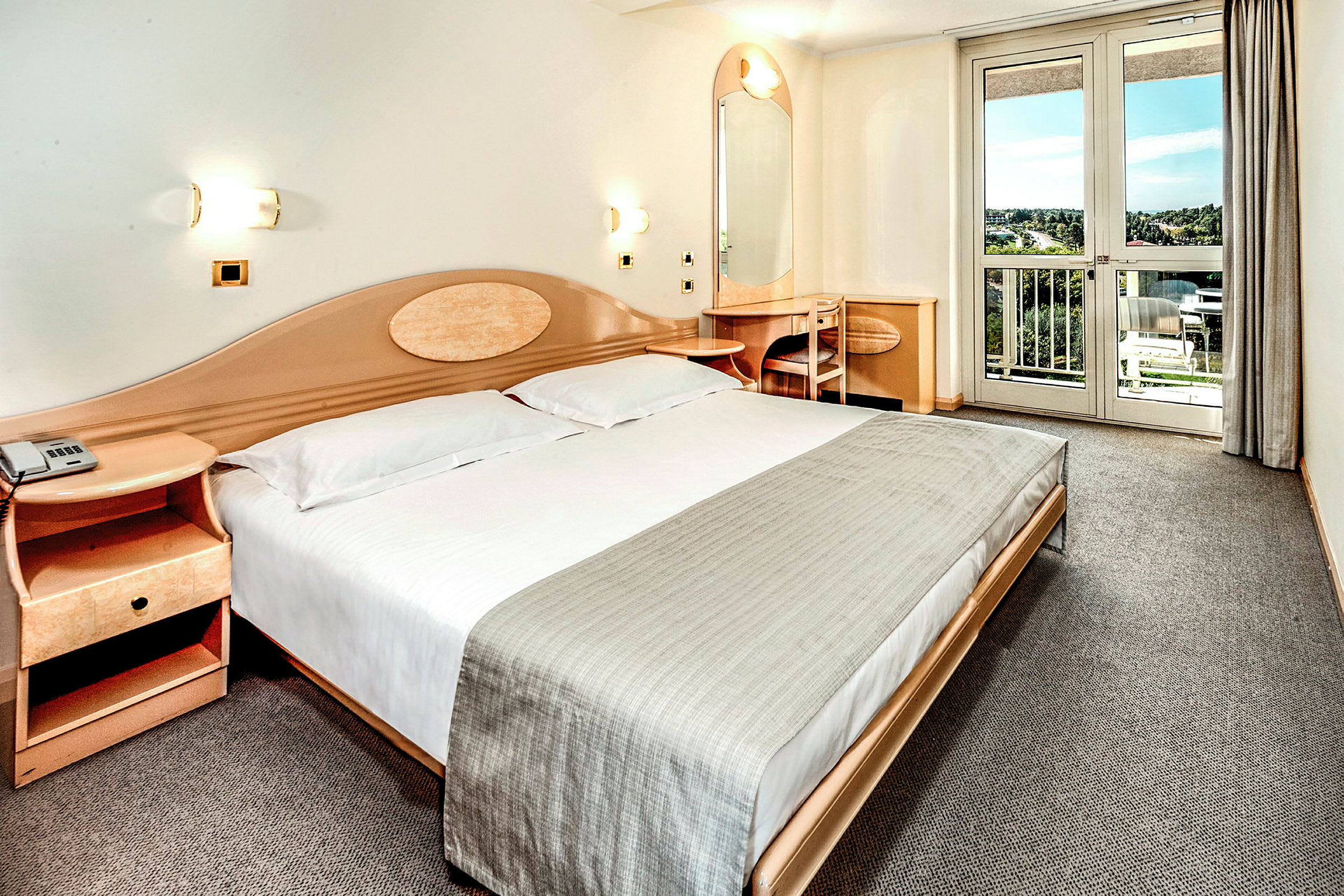 Ett hotellrum med en dubbelsäng, en nattduksbord, ett skrivbord och en balkong med utsikt. (AI-genererad text)