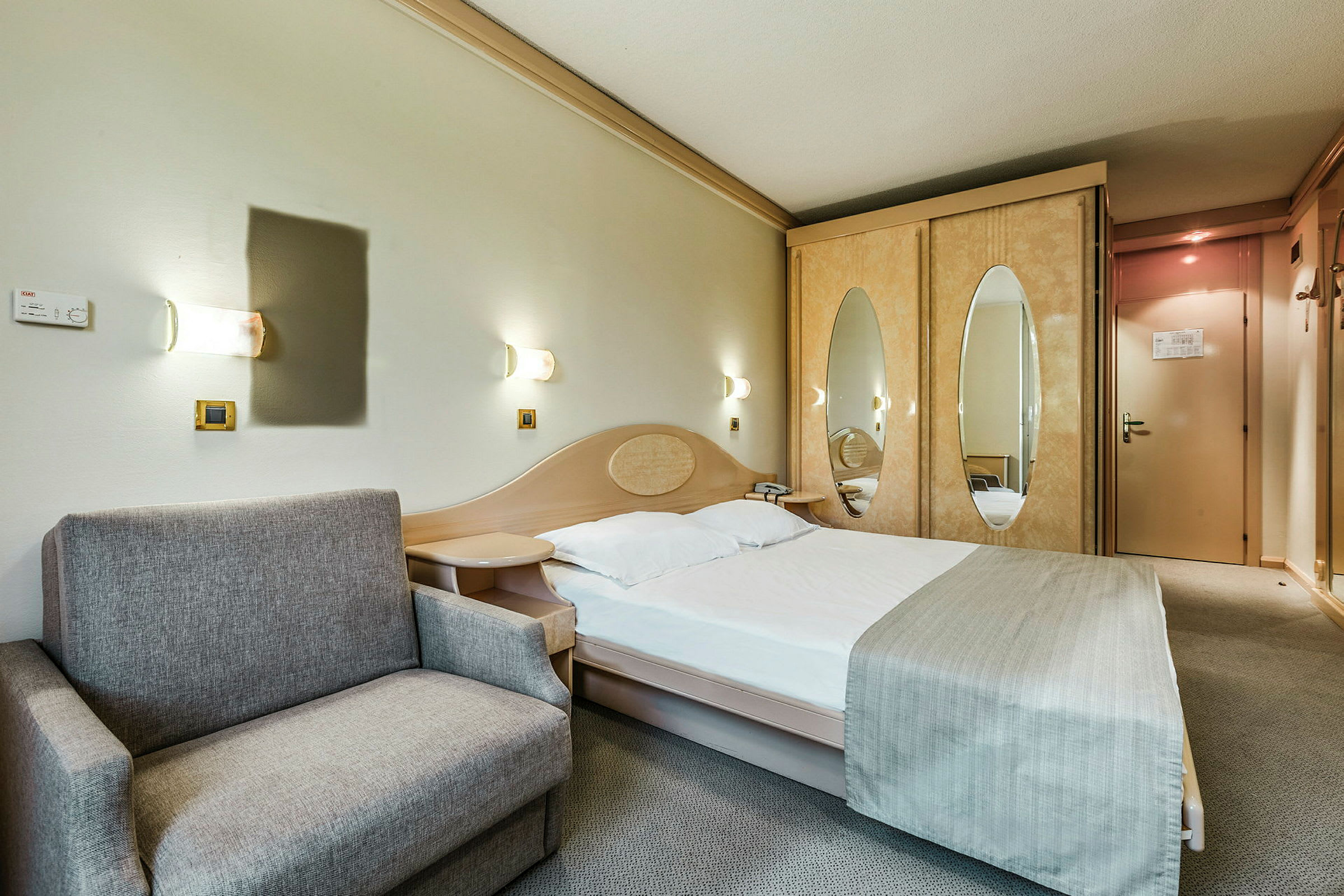 Ett hotellrum med en bäddad säng, en grå soffa och en garderob med speglade dörrar. (AI-genererad text)