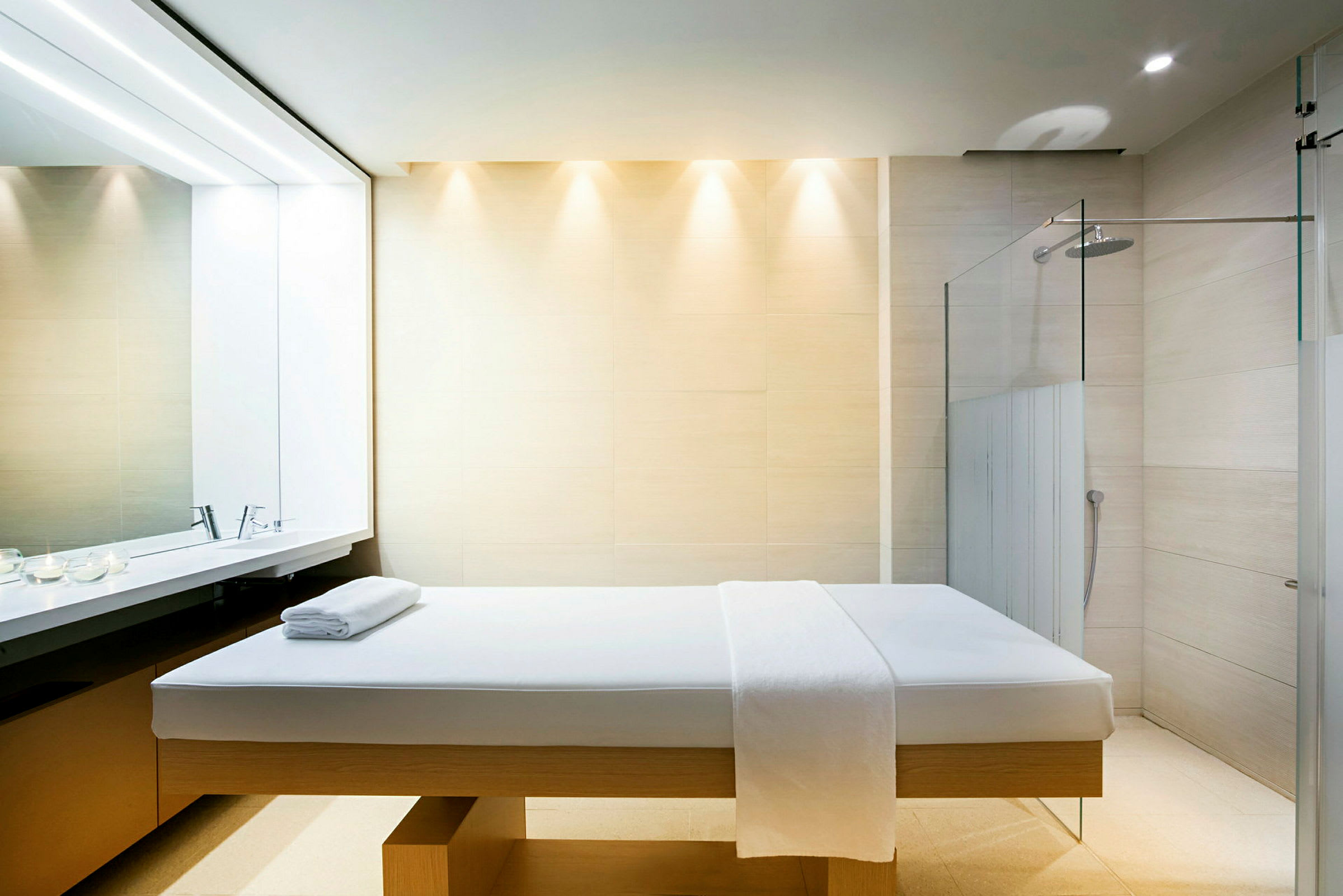 Ett spa-rum med en massagebrits, handdukar och en dusch i bakgrunden. (AI-genererad text)