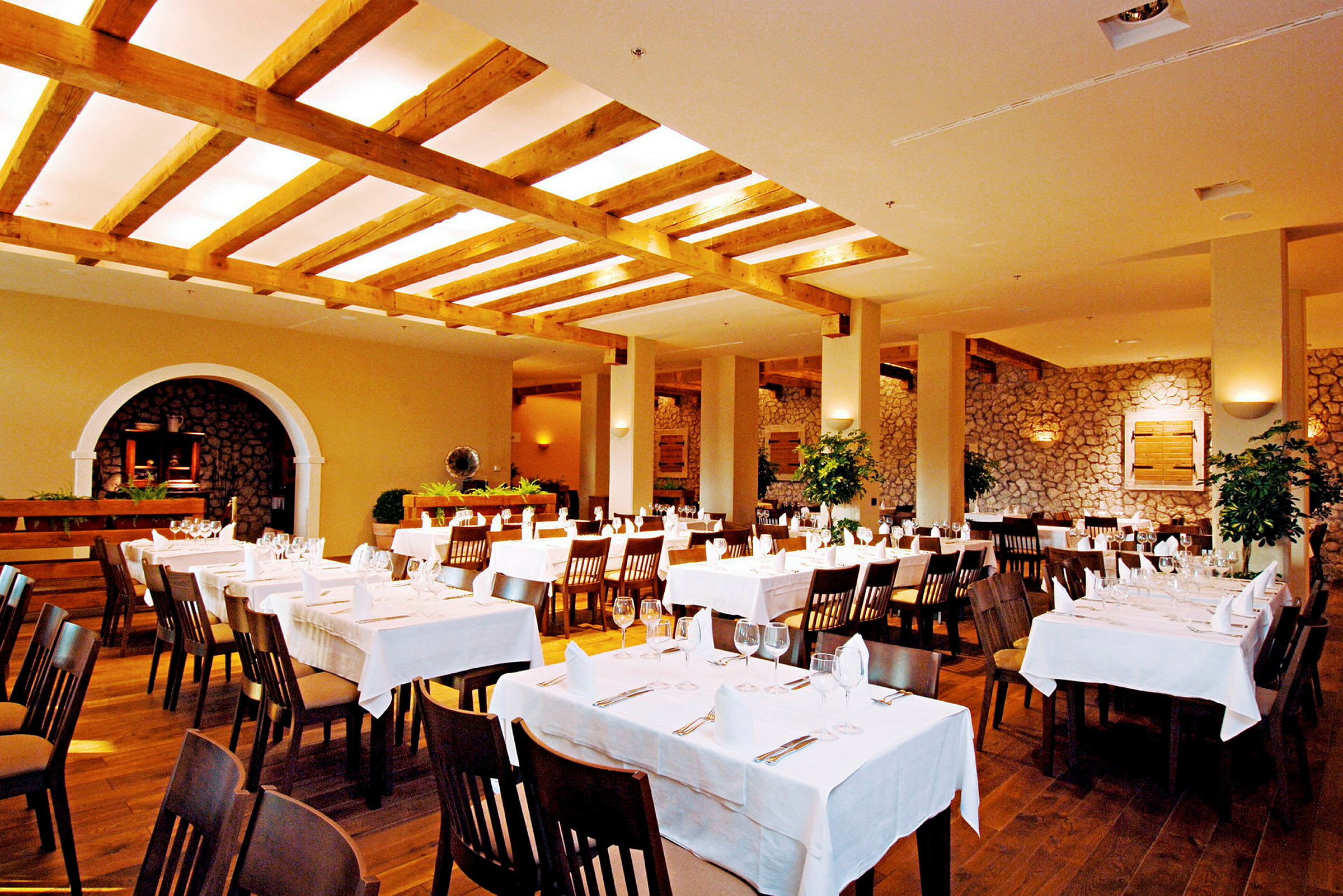En restaurang med dukade bord och vita dukar i en rymlig lokal med träbjälkar i taket. (AI-genererad text)