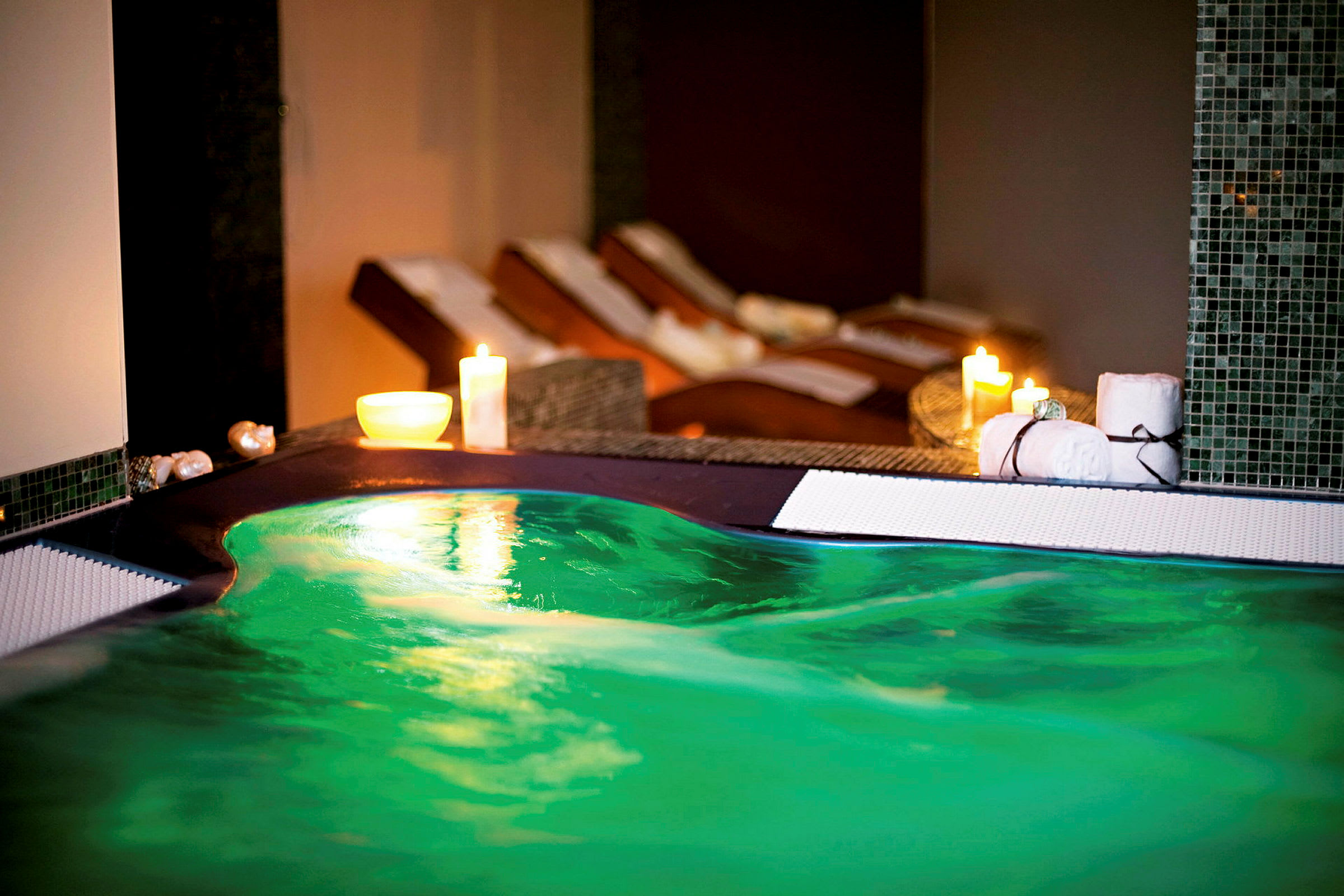 Bild av en jacuzzi med grönt vatten och levande ljus i en spa-liknande miljö. Det finns handdukar och avkopplingsutrustning i bakgrunden. (AI-genererad text)