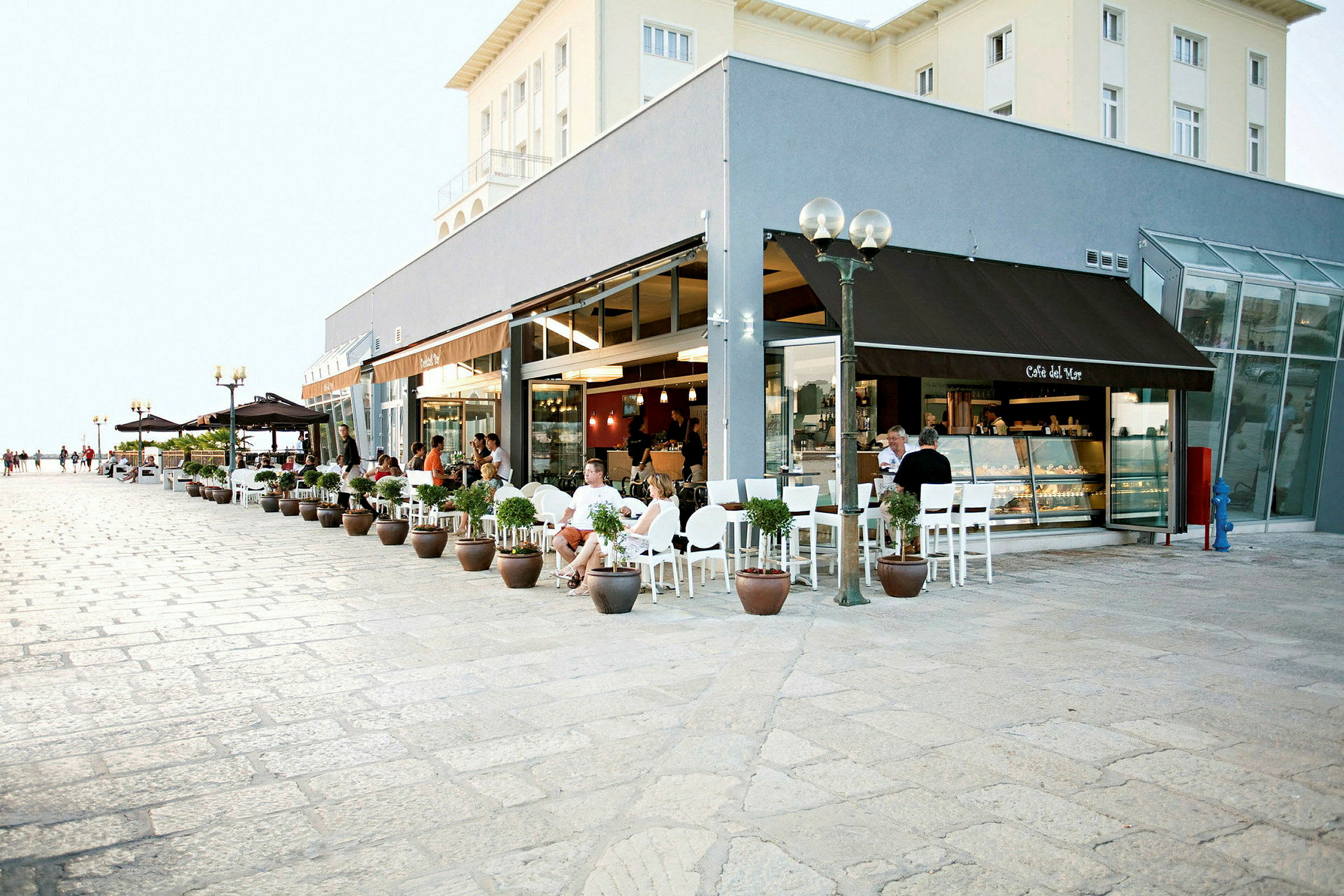 Bild av ett kafé med uteservering och krukväxter längs en stenbelagd gångväg. (AI-genererad text)