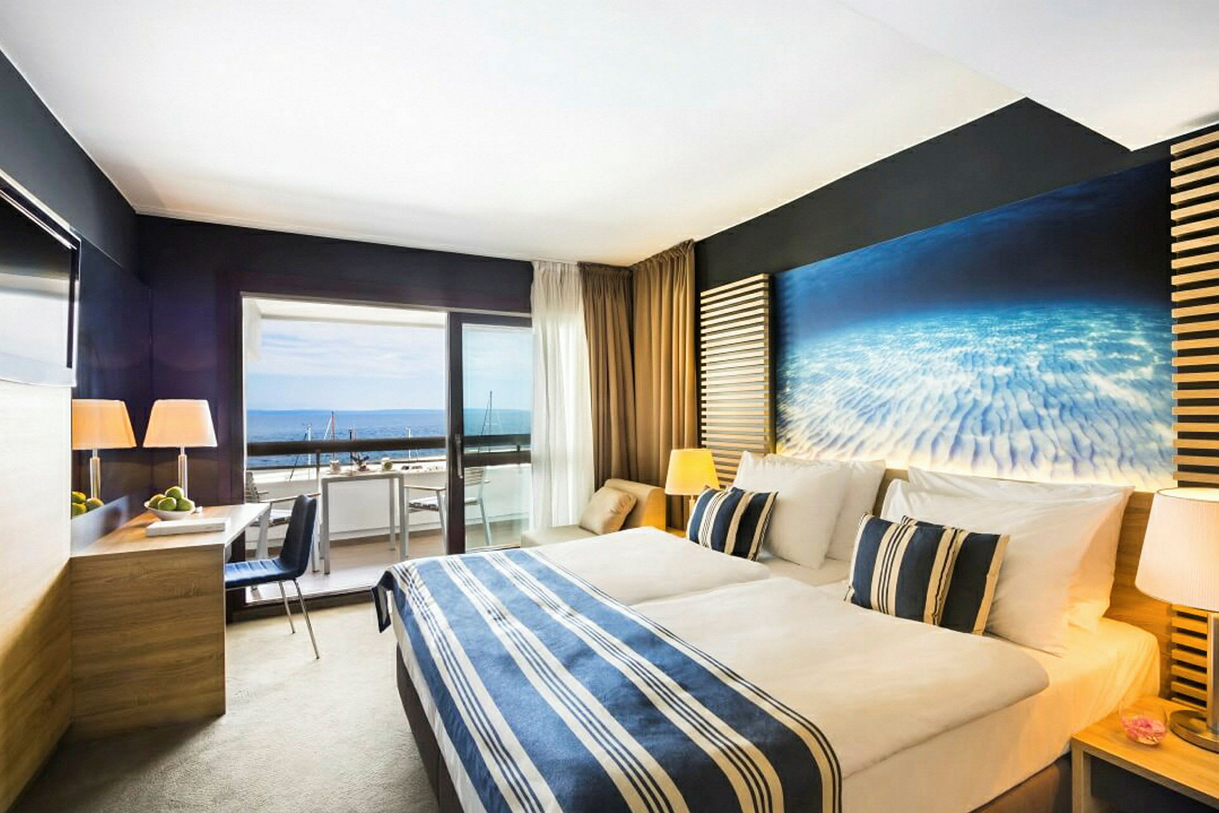 Ett hotellrum med en dubbelsäng, moderna möbler och en balkong som vetter mot havet. (AI-genererad text)