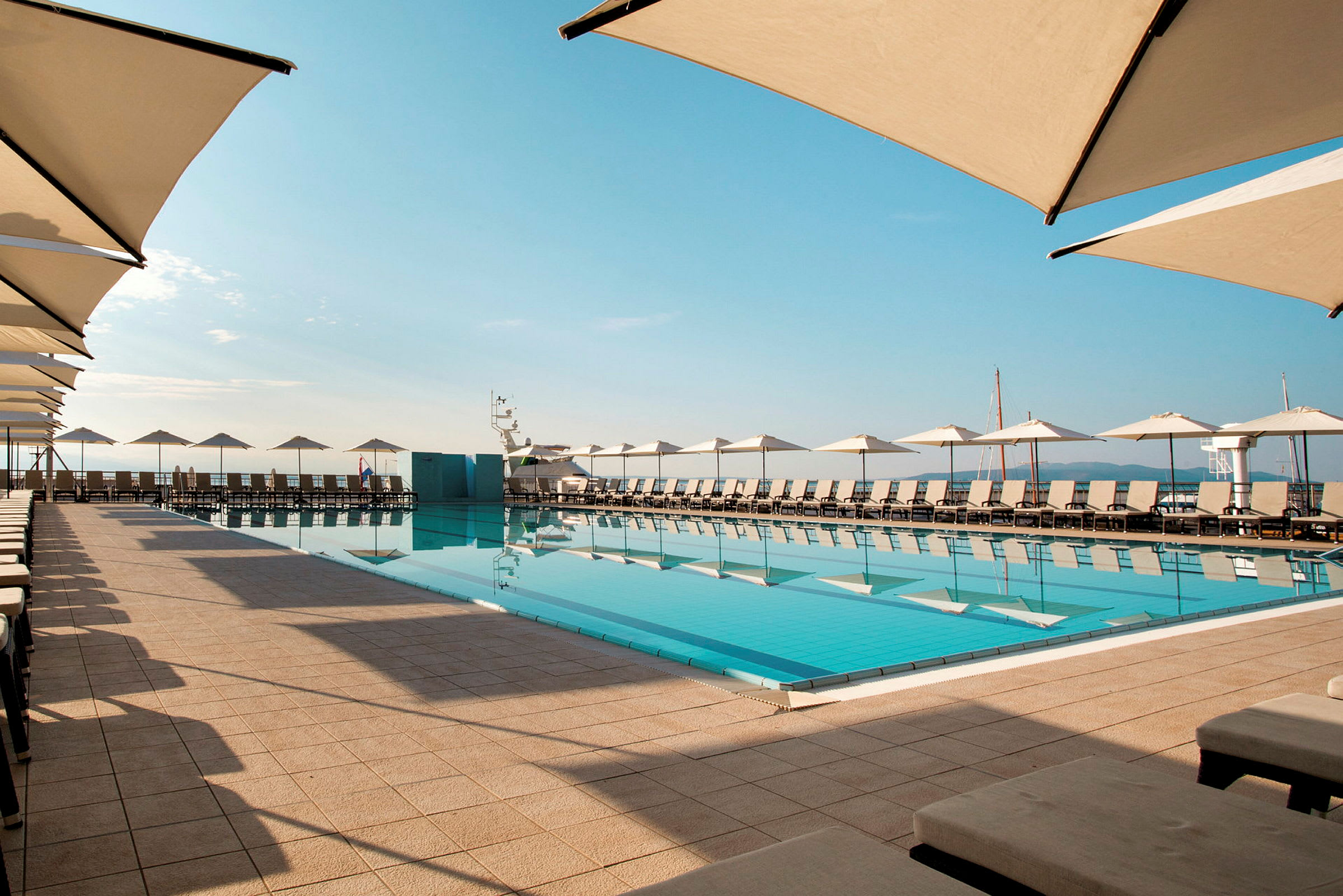 En swimmingpool med solstolar och parasoller runtom, belägen utomhus under en blå himmel. (AI-genererad text)