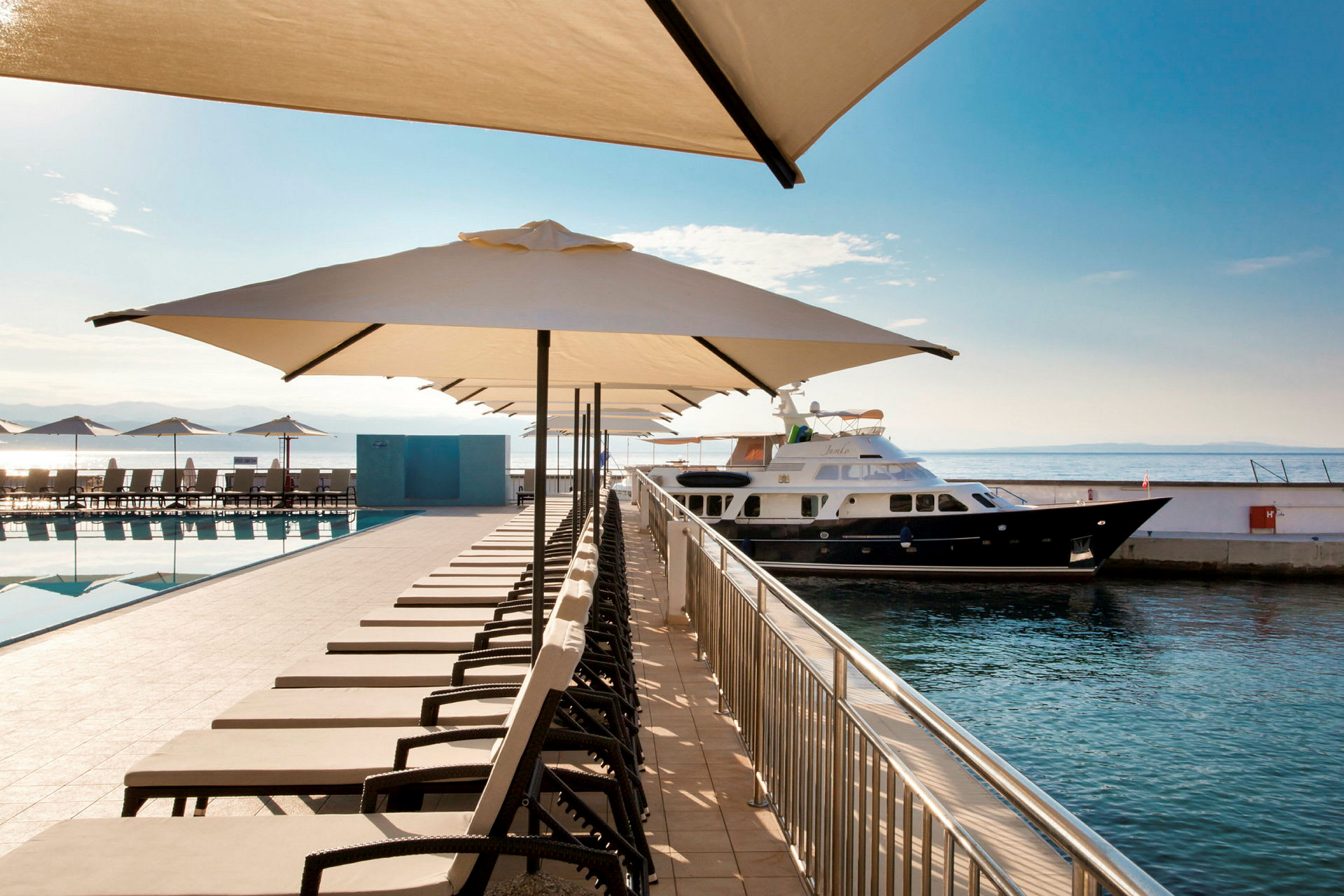 Solstolar och parasoller vid en pool intill en yacht vid kajen. (AI-genererad text)
