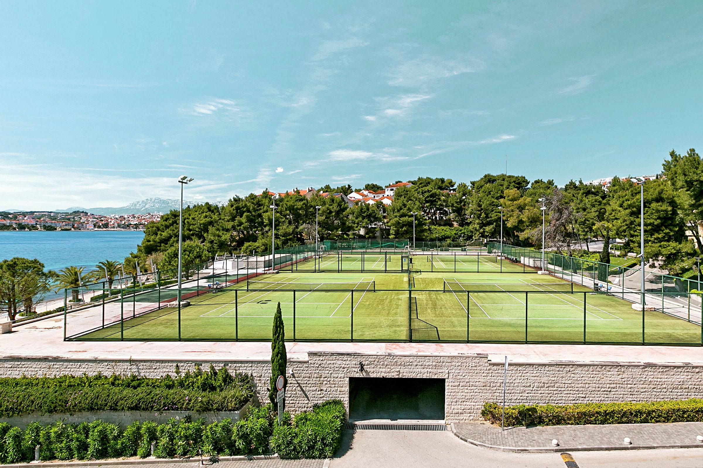 Bild av tennisplaner utomhus med hav och byggnader i bakgrunden. (AI-genererad text)