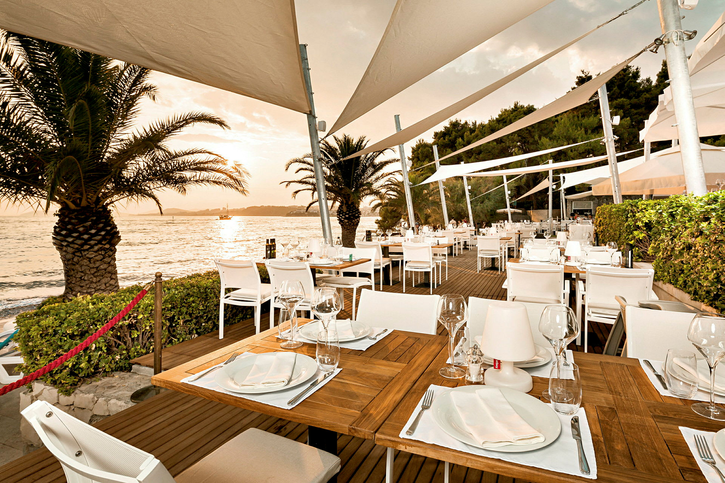 En utomhusrestaurang med dukade bord och havsutsikt vid solnedgång. (AI-genererad text)