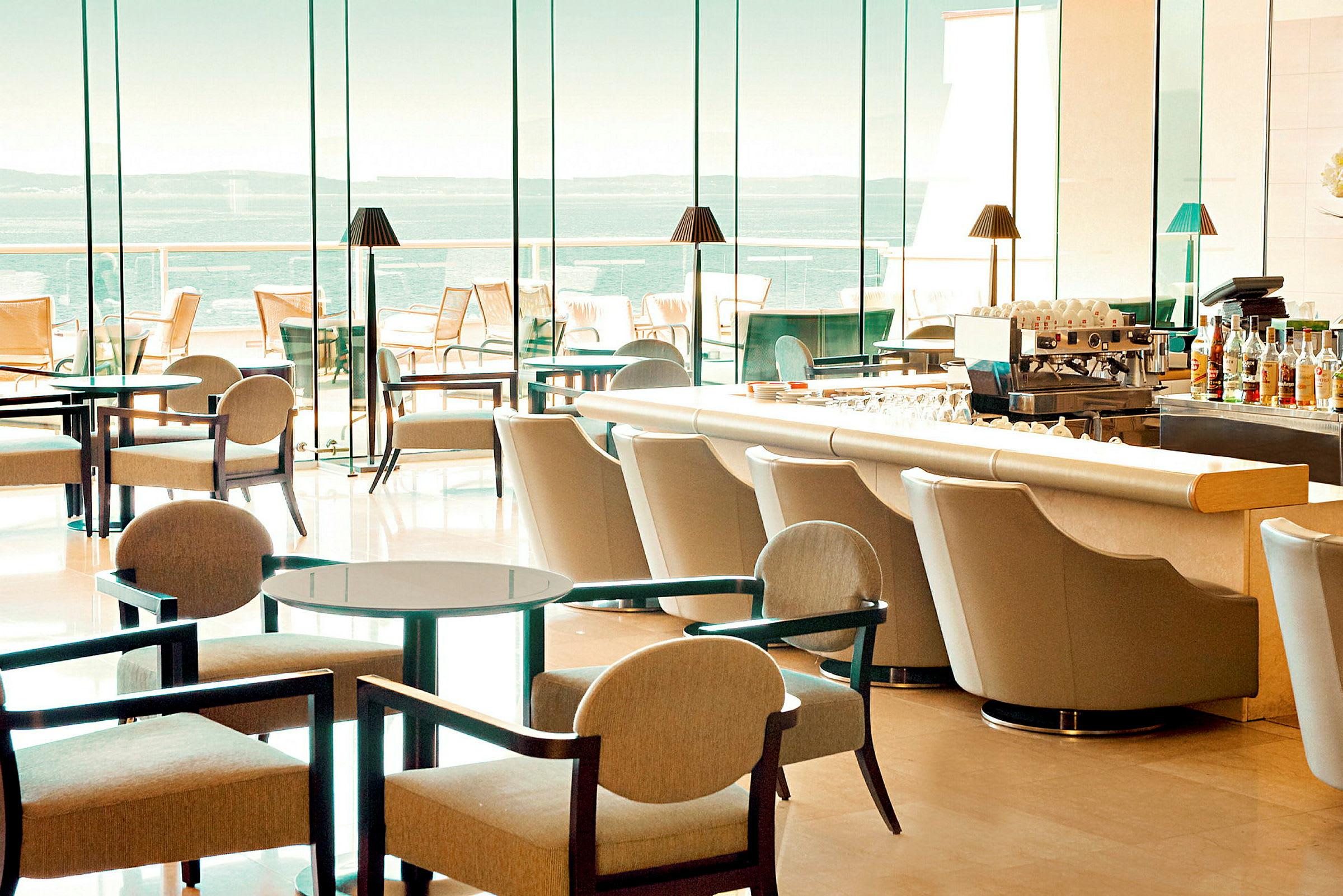 Hotellbar med moderna möbler och stora glasfönster med utsikt över havet. (AI-genererad text)
