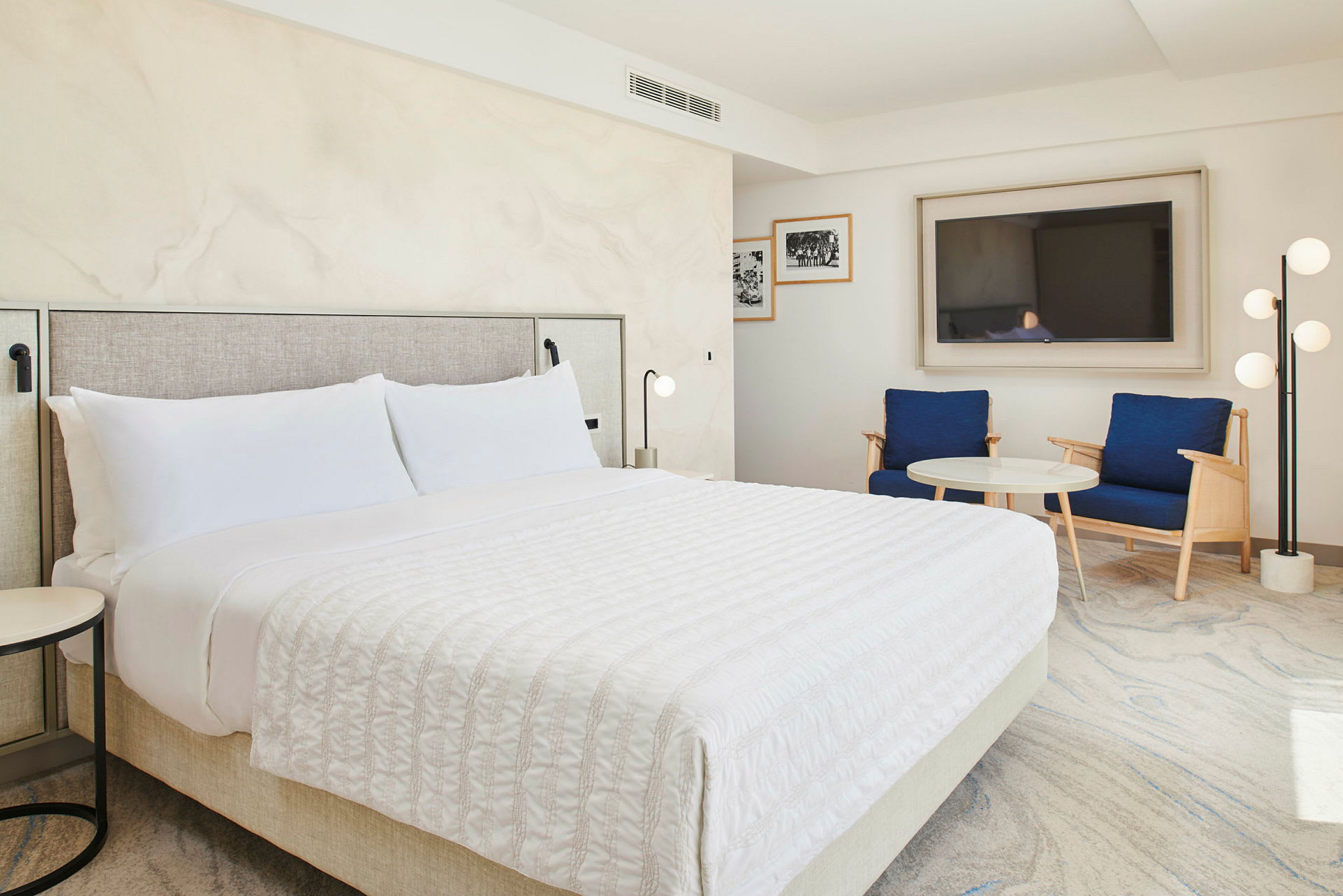 Ett hotellrum med en dubbelsäng, två blå fåtöljer och ett soffbord. (AI-genererad text)