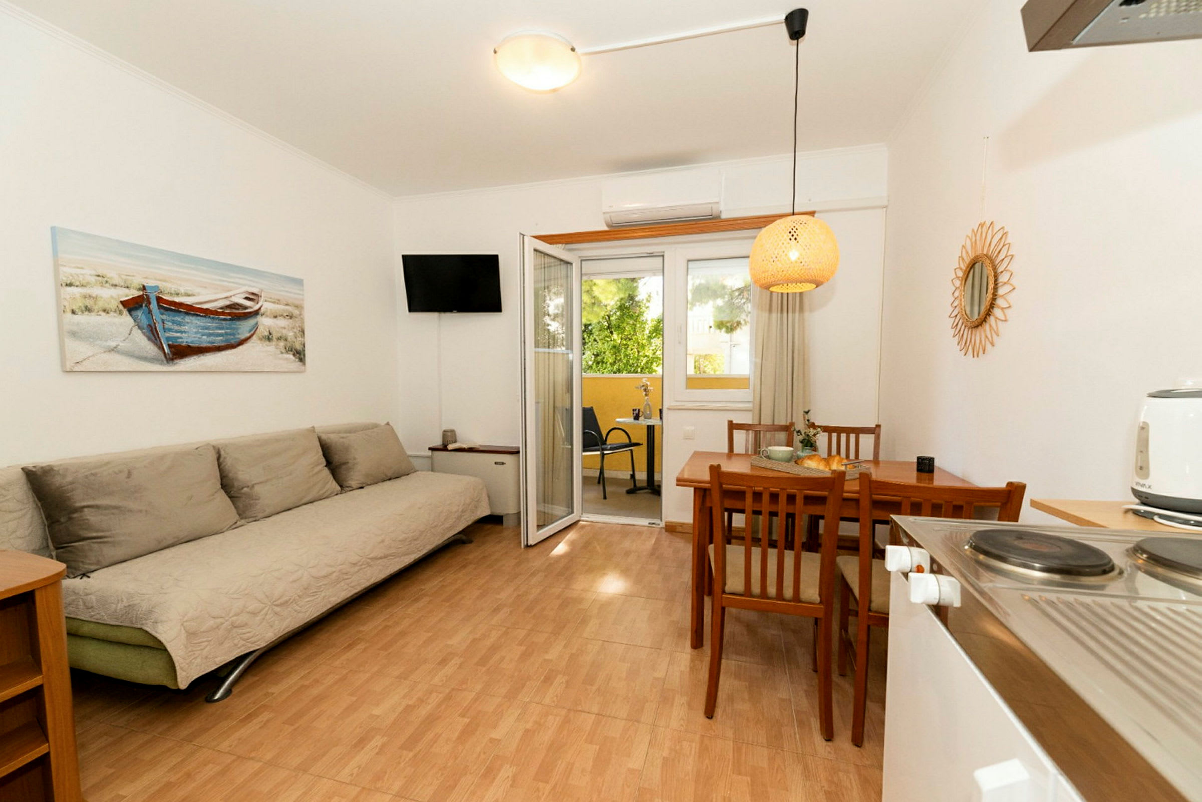Ett rum med en soffa, matbord med stolar och dörrar som leder till en balkong. En tavla med en båt hänger på väggen. (AI-genererad text)
