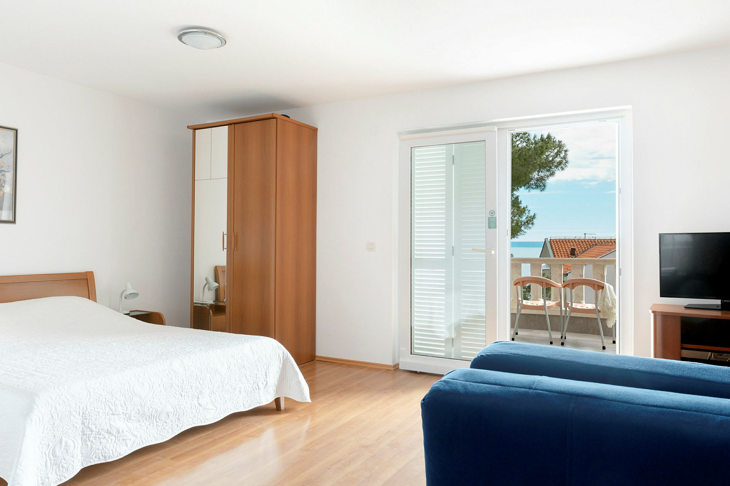 Ett hotellrum med säng, garderob, blå soffa, TV och balkong med utsikt. (AI-genererad text)