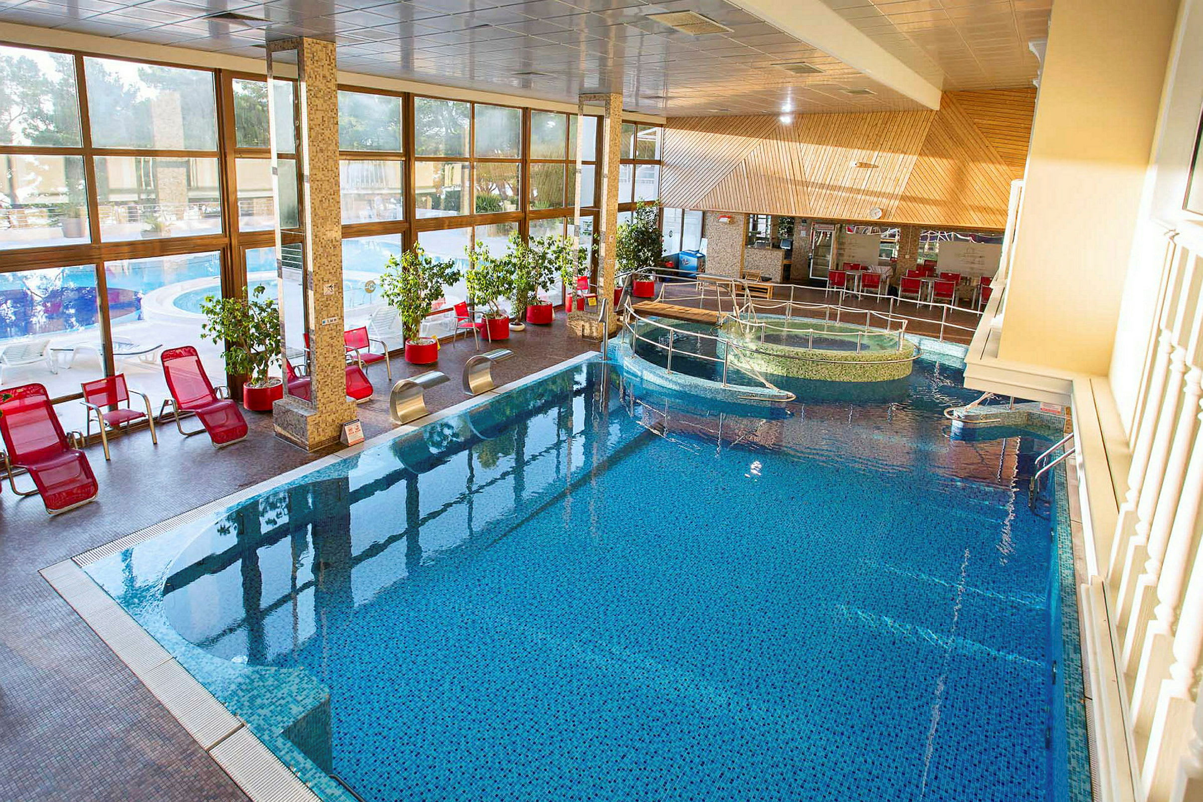 Inomhuspool med röda solstolar och stora fönster med utsikt. (AI-genererad text)