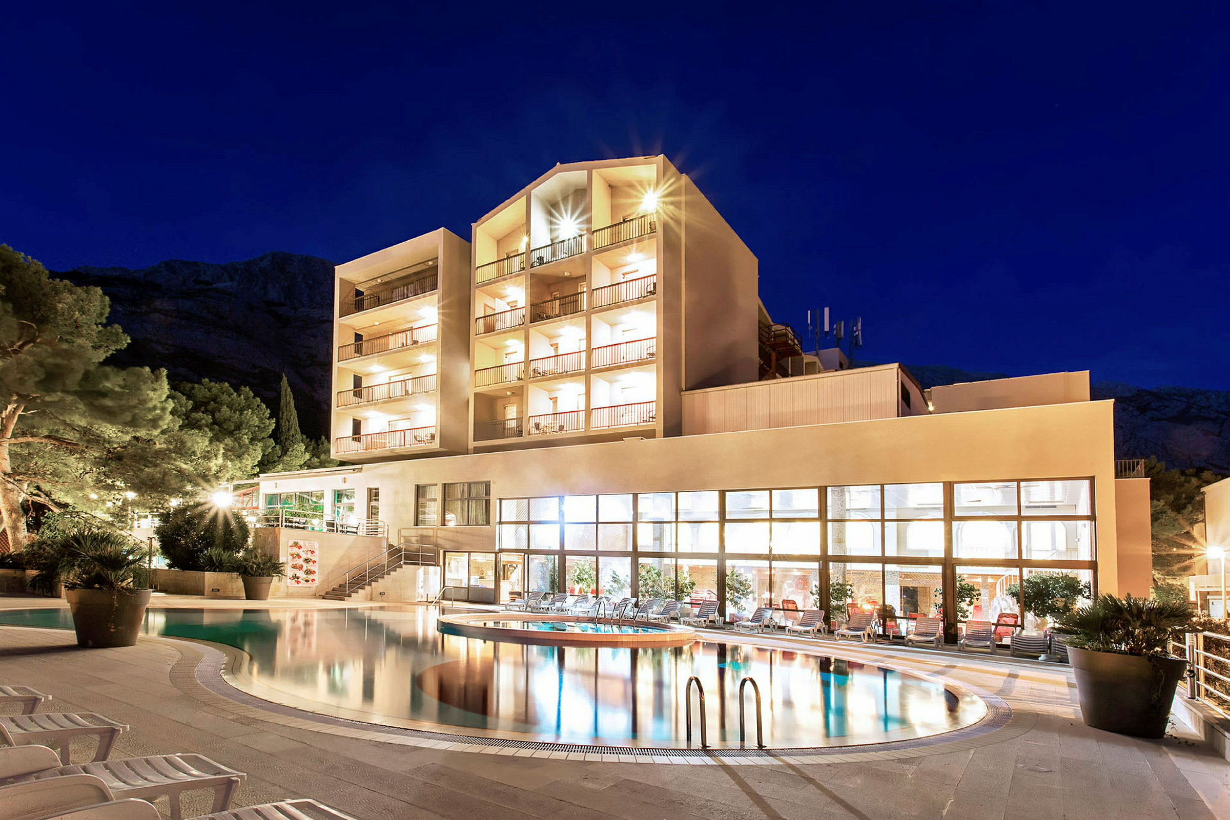 Ett hotell med en upplyst fasad vid en pool under natten. (AI-genererad text)