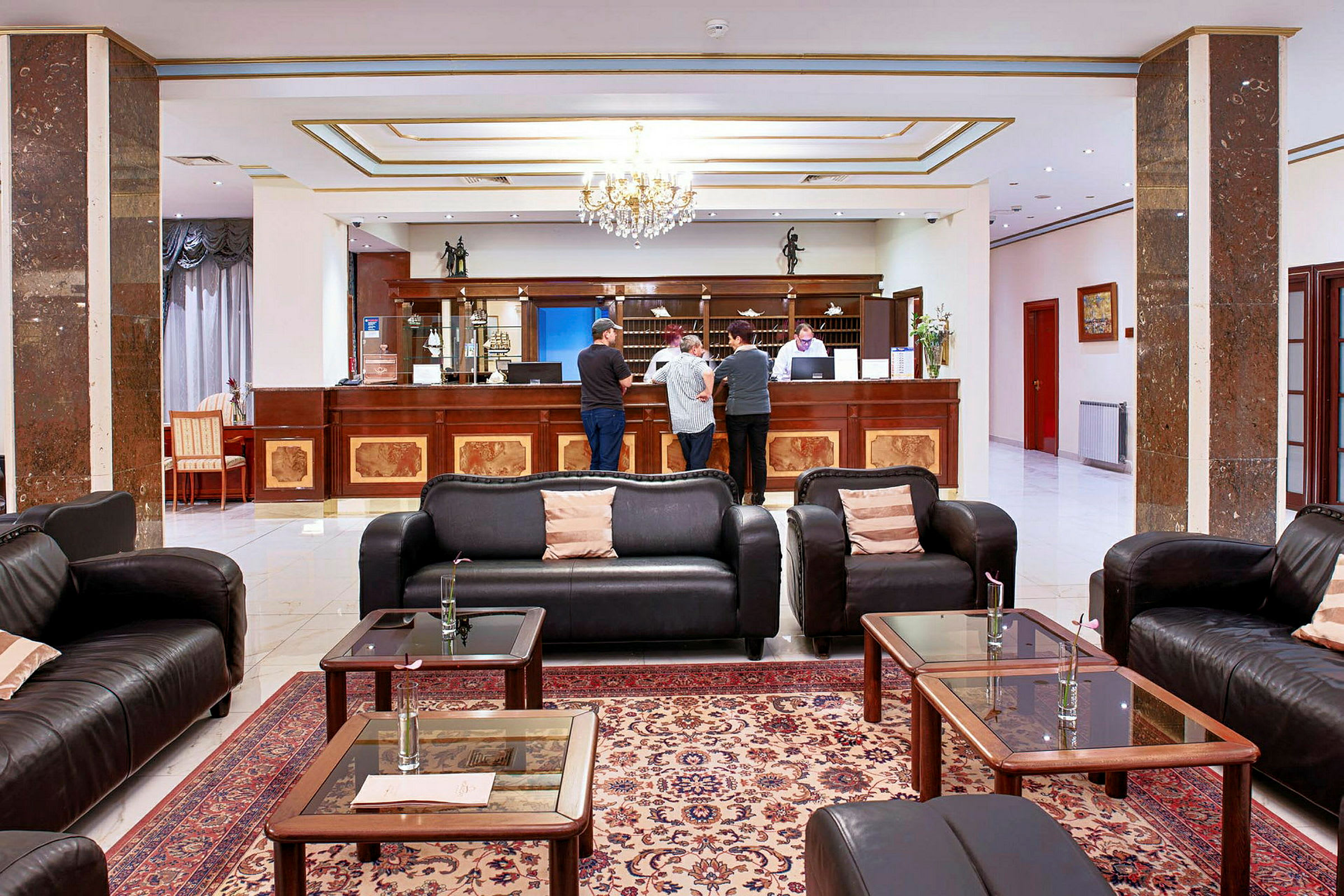 Hotellobby med soffor, soffbord och receptionsdisk där flera personer står. (AI-genererad text)