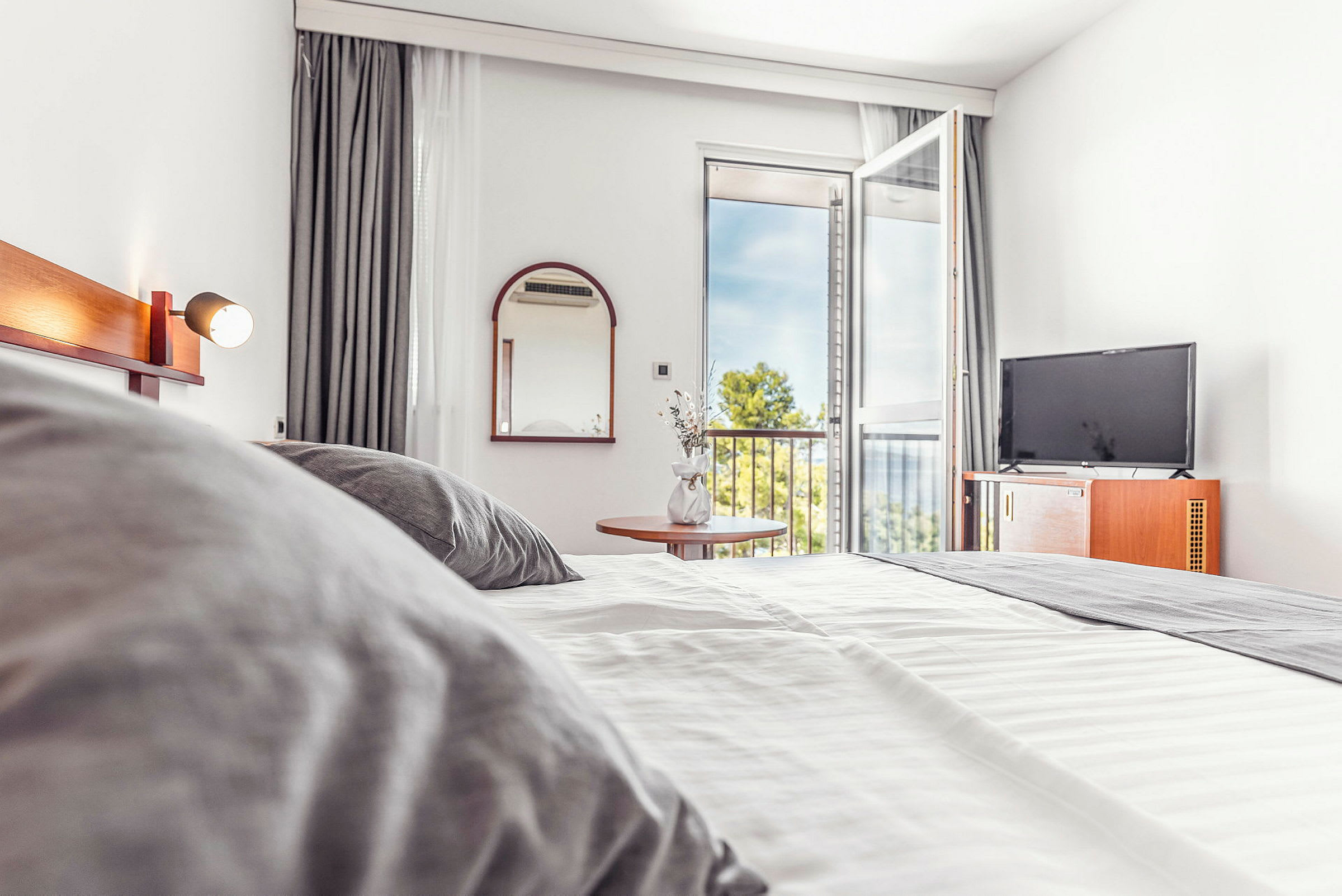 Hotellrum med säng, TV och öppen balkongdörr. (AI-genererad text)