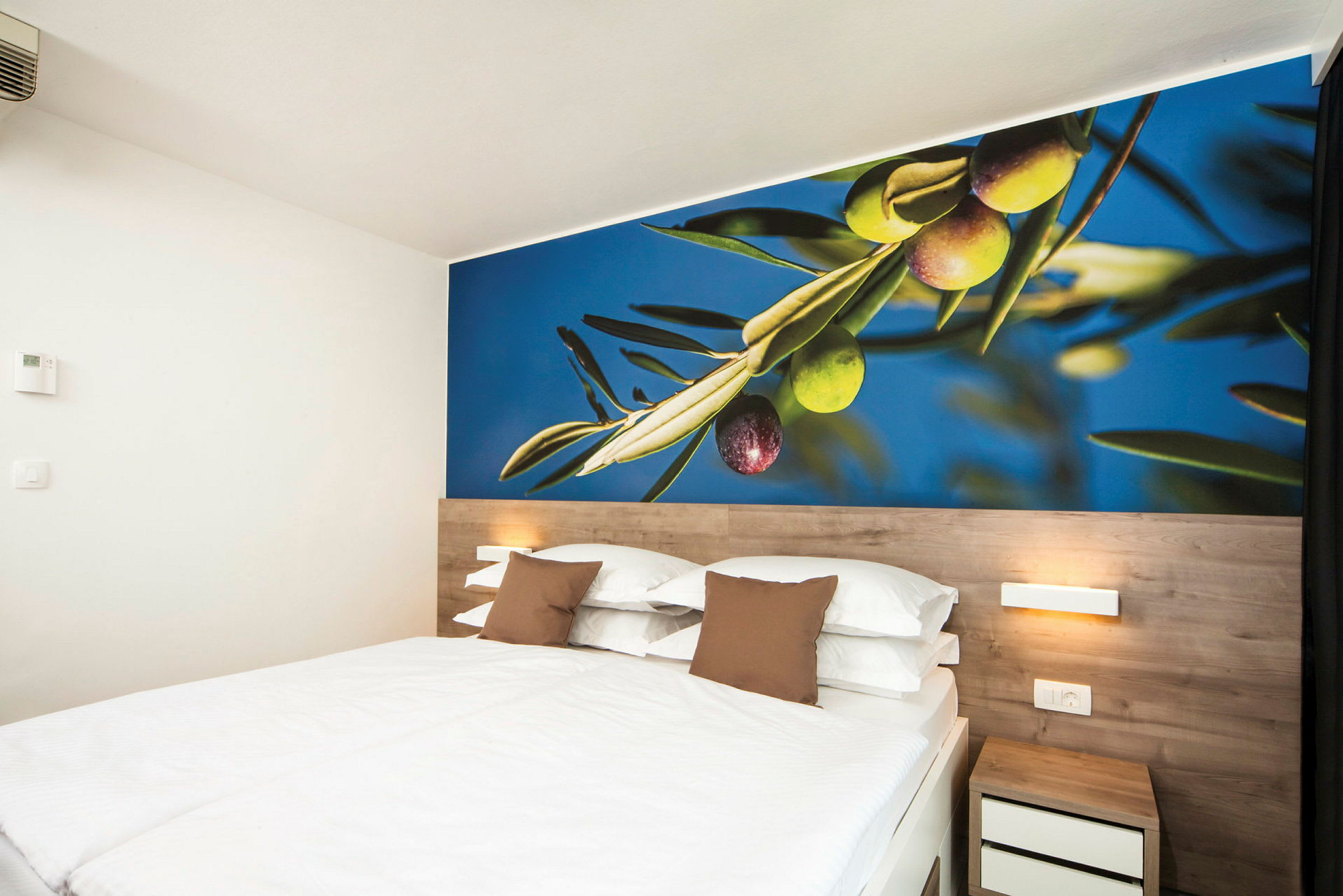 Ett hotellrum med en dubbelsäng och en väggmålning av oliver. (AI-genererad text)