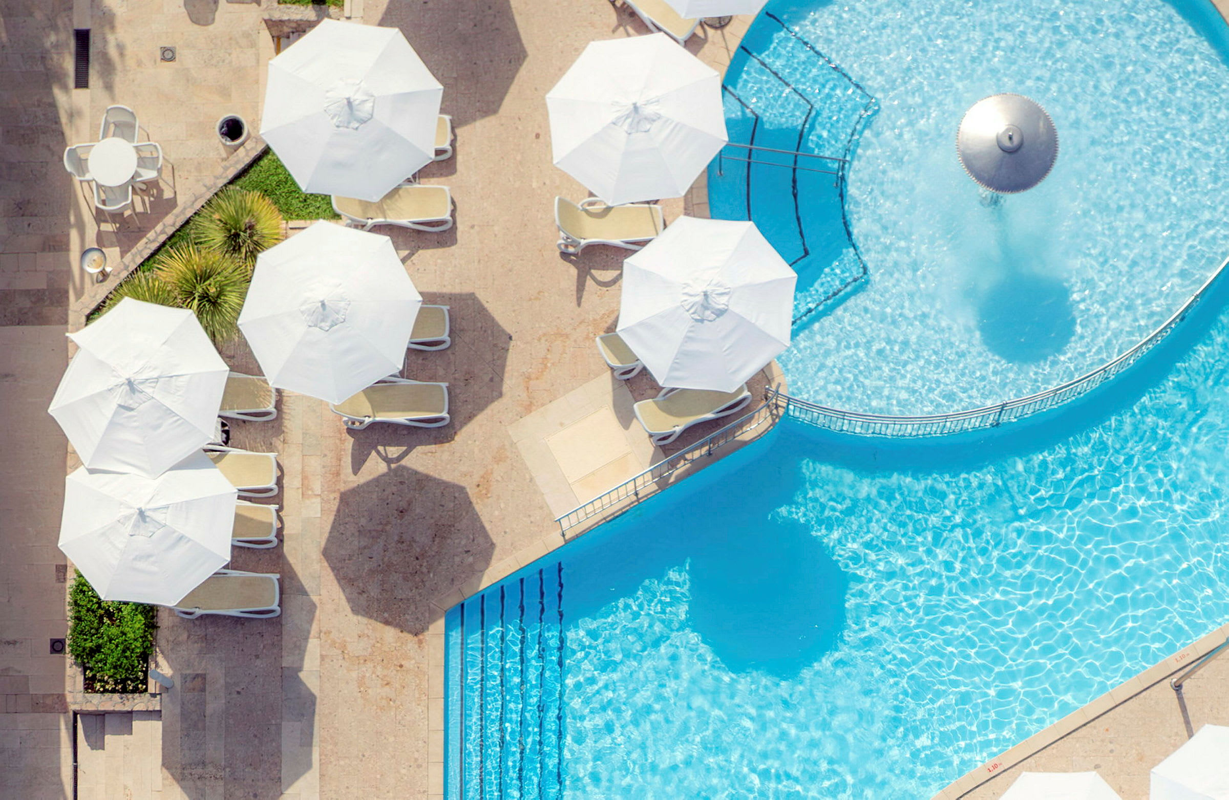 Vy över en pool med parasoller och solstolar samt ett bord. (AI-genererad text)