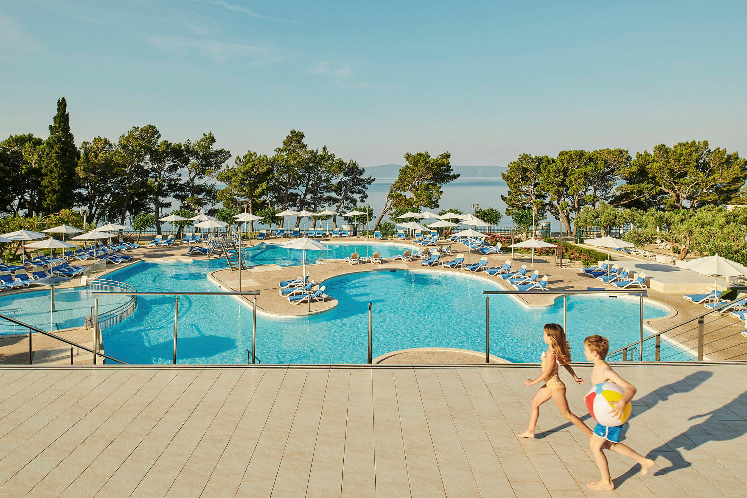 Utsikt över en pool med solstolar och parasoller, omgiven av grönska. (AI-genererad text)