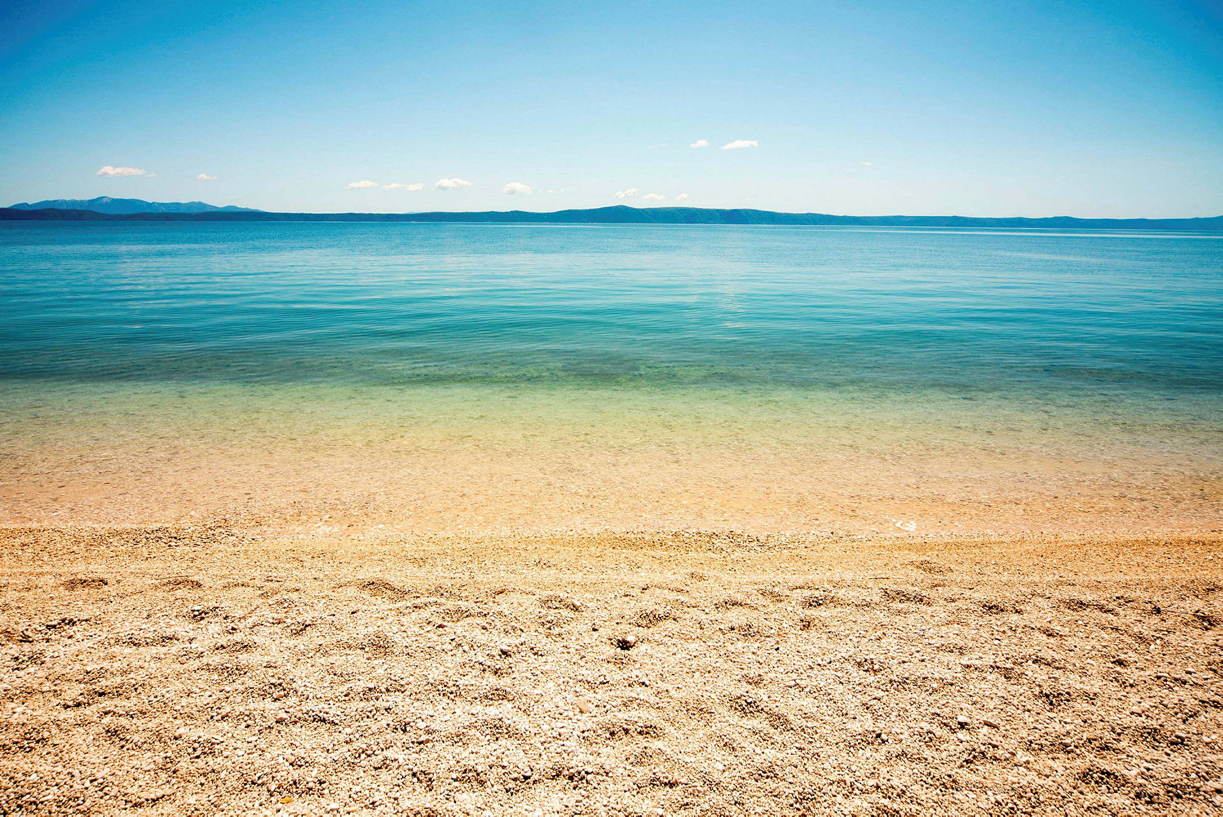 En strand med småsten vid klart vatten och en fjärran horisont. (AI-genererad text)