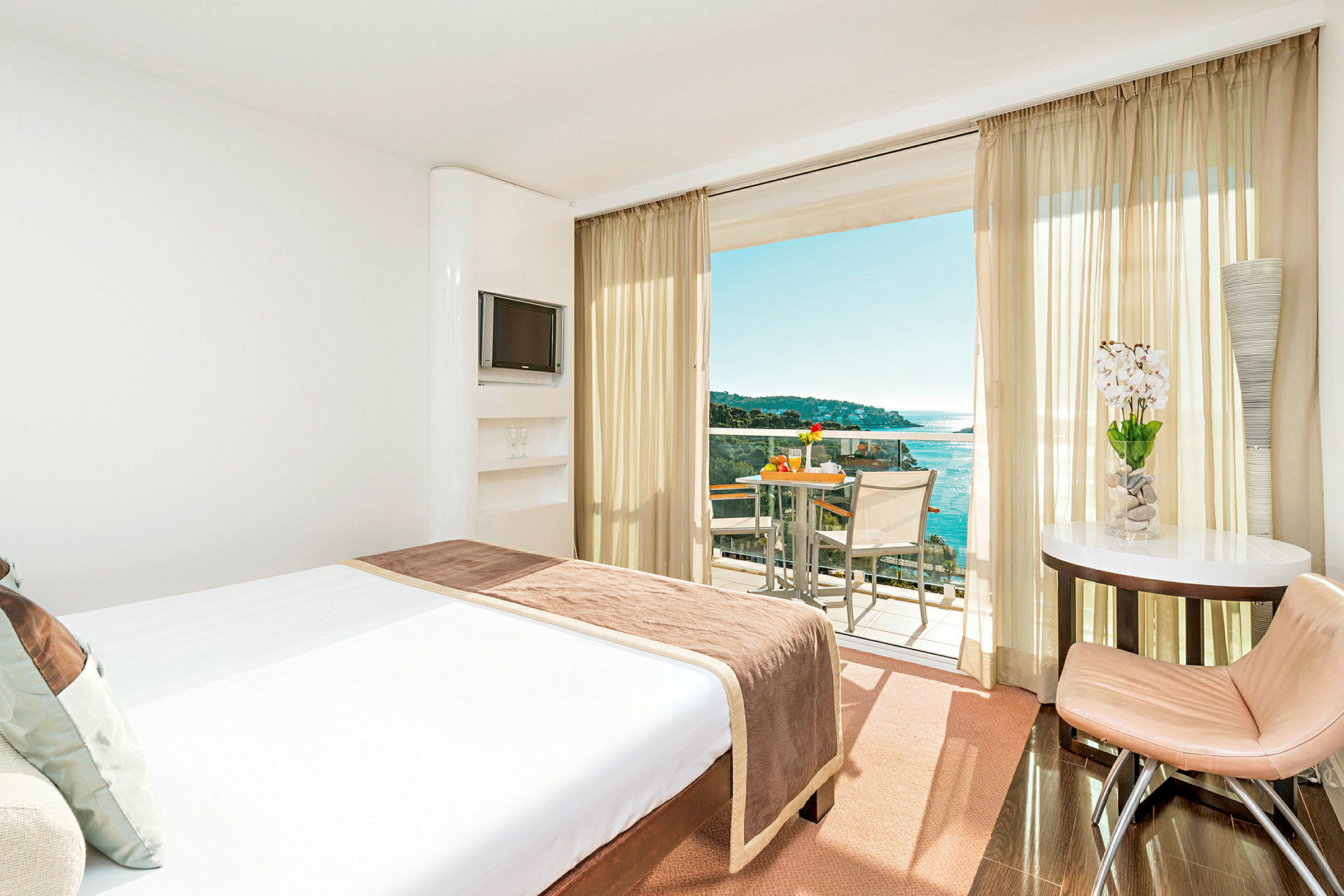 Hotellrum med en stor säng som vetter mot en balkong med utsikt över havet. (AI-genererad text)