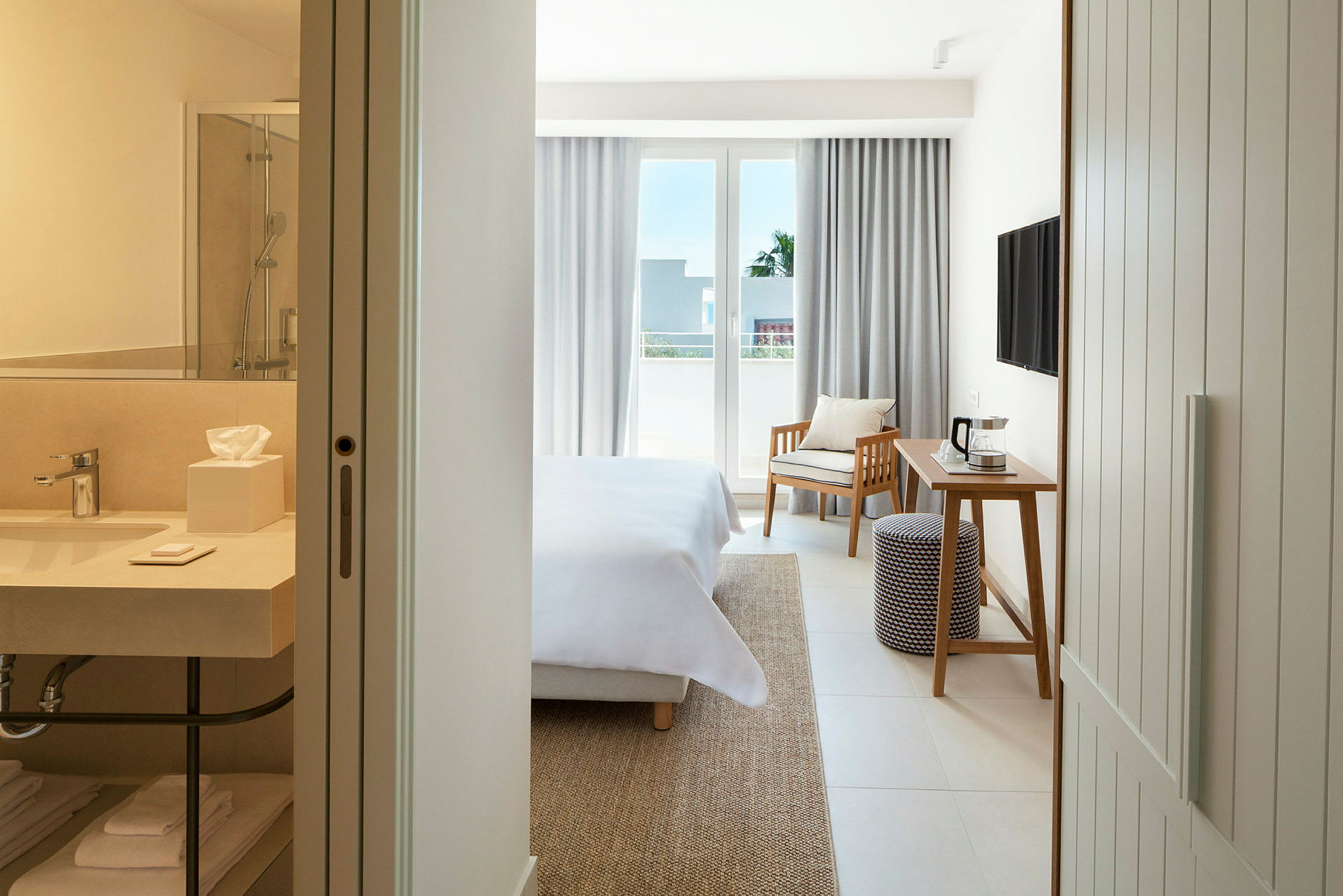 Ett hotellrum med en säng, ett skrivbord, en stol och en balkong. I förgrunden syns ett badrum. (AI-genererad text)