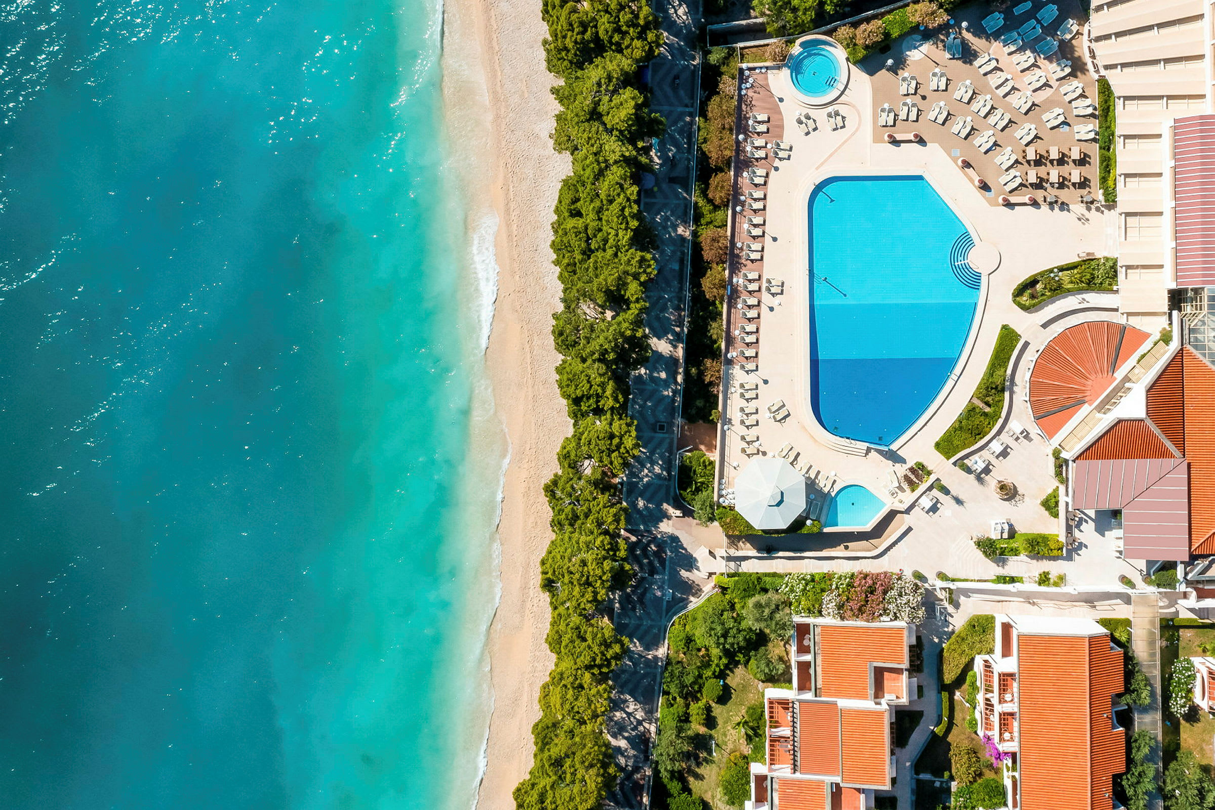 Luftvy av en strand, swimmingpool och hotellbyggnader. (AI-genererad text)