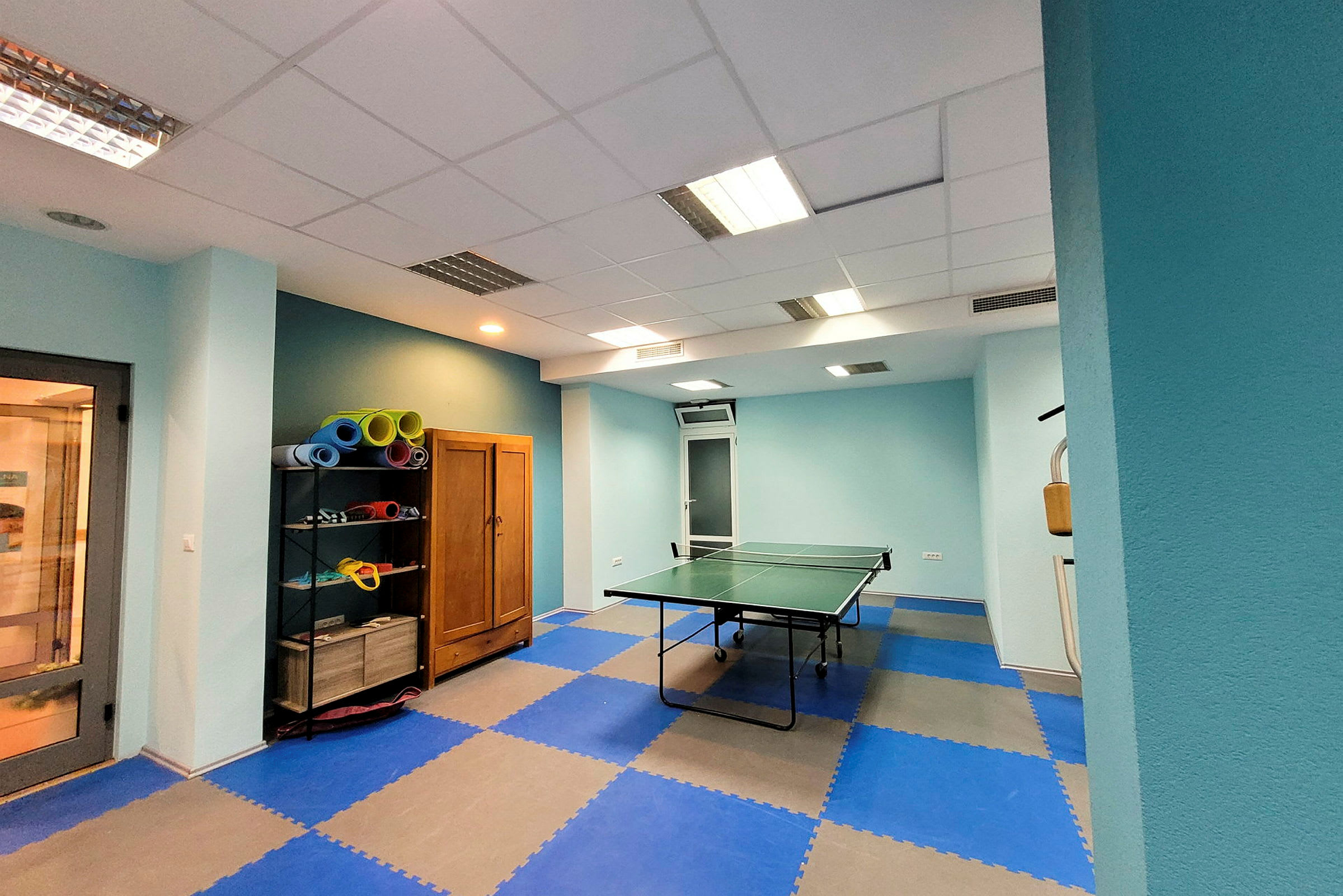 En bild av ett rum med bordtennisbord och hylla med yogamattor. (AI-genererad text)