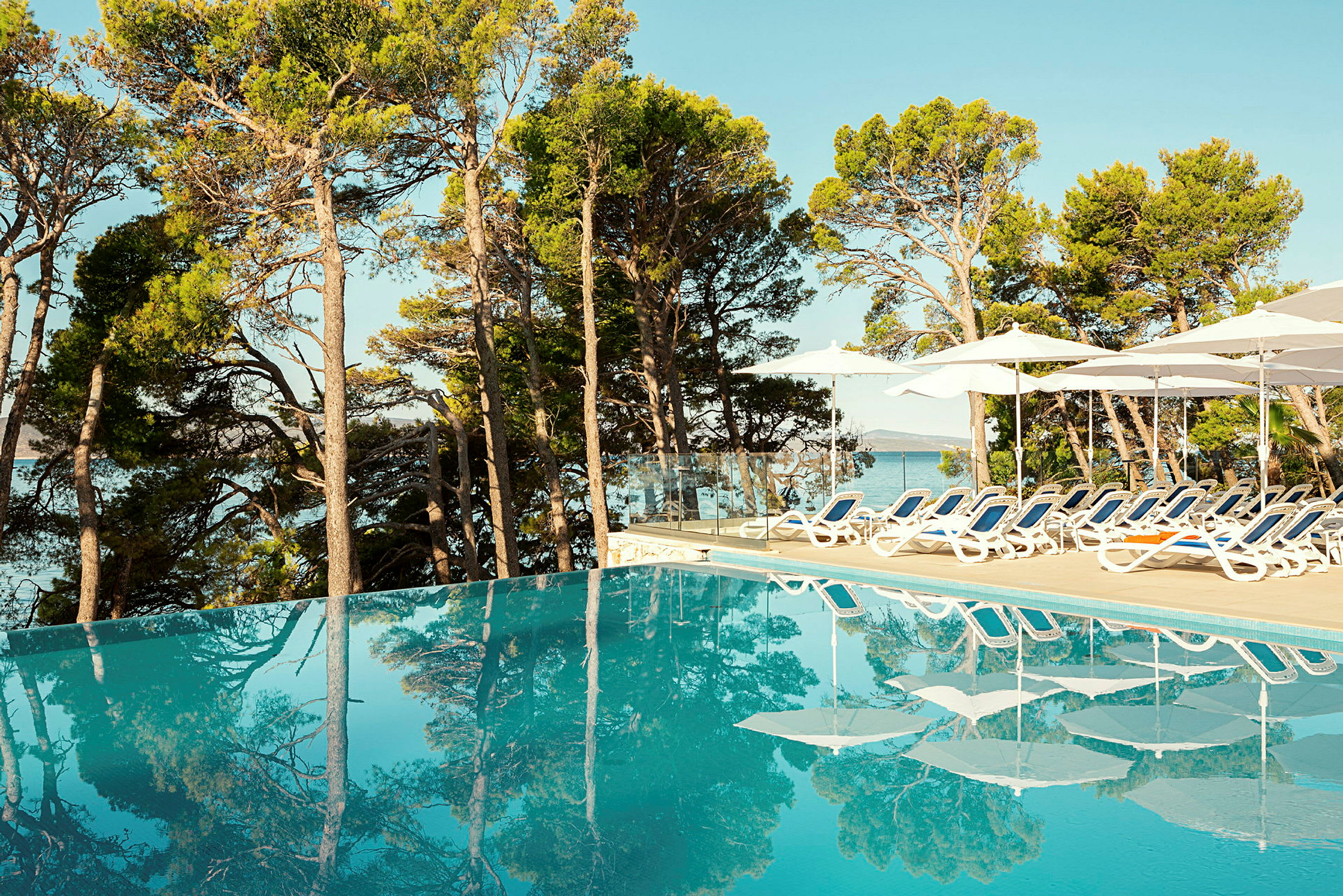 Infinitypool omgiven av solstolar och parasoller, med utsikt över skog och hav. (AI-genererad text)