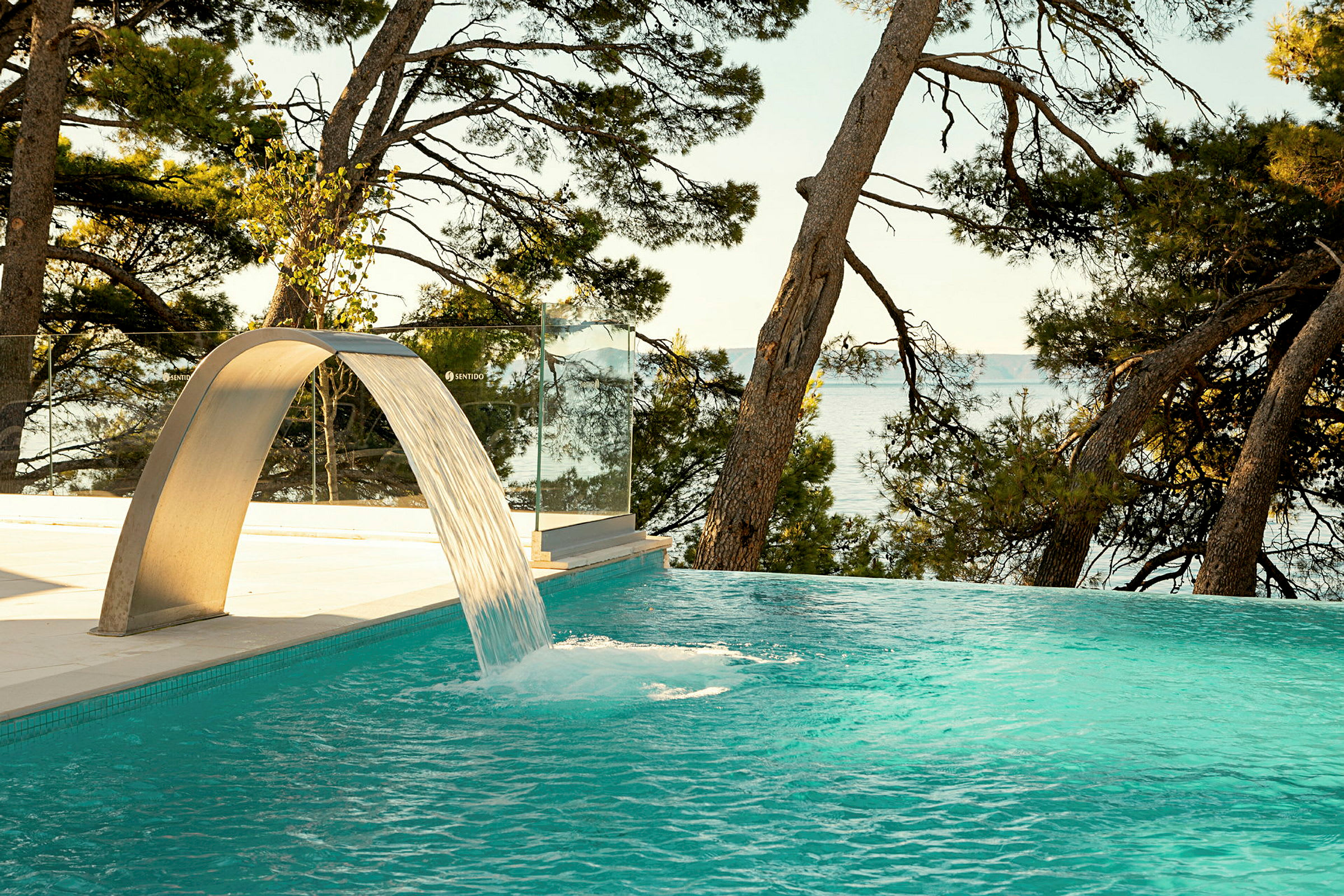 Infinitypool med vattenfall samt med utsikt mot hav och tallar. (AI-genererad text)