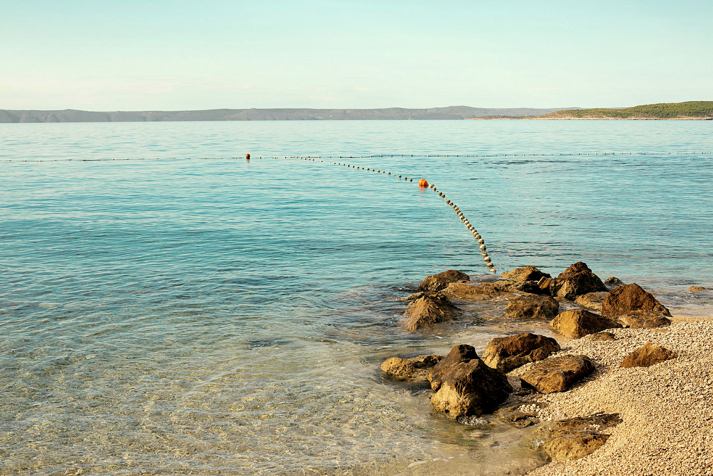 En stenig strand med stilla, klart vatten som sträcker sig mot horisonten. (AI-genererad text)