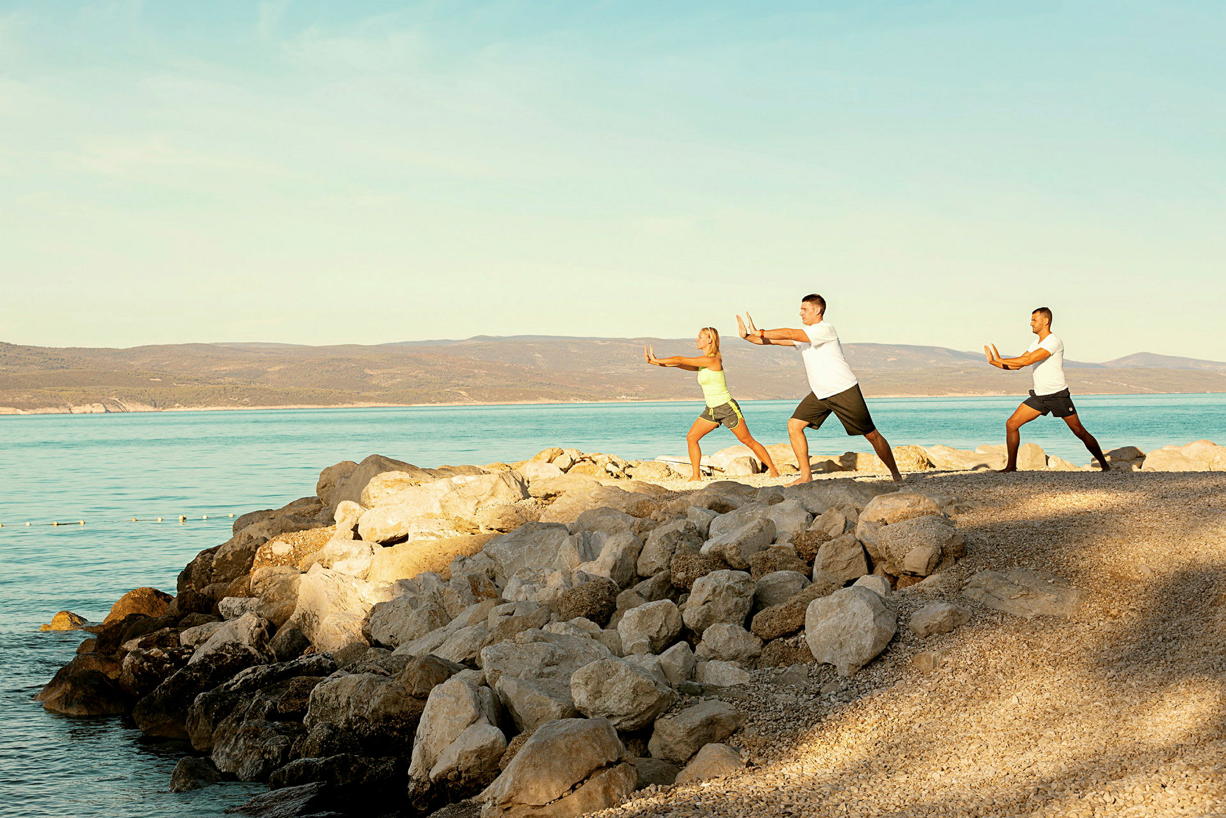 Tre personer utövar tai chi vid stranden intill havet. (AI-genererad text)