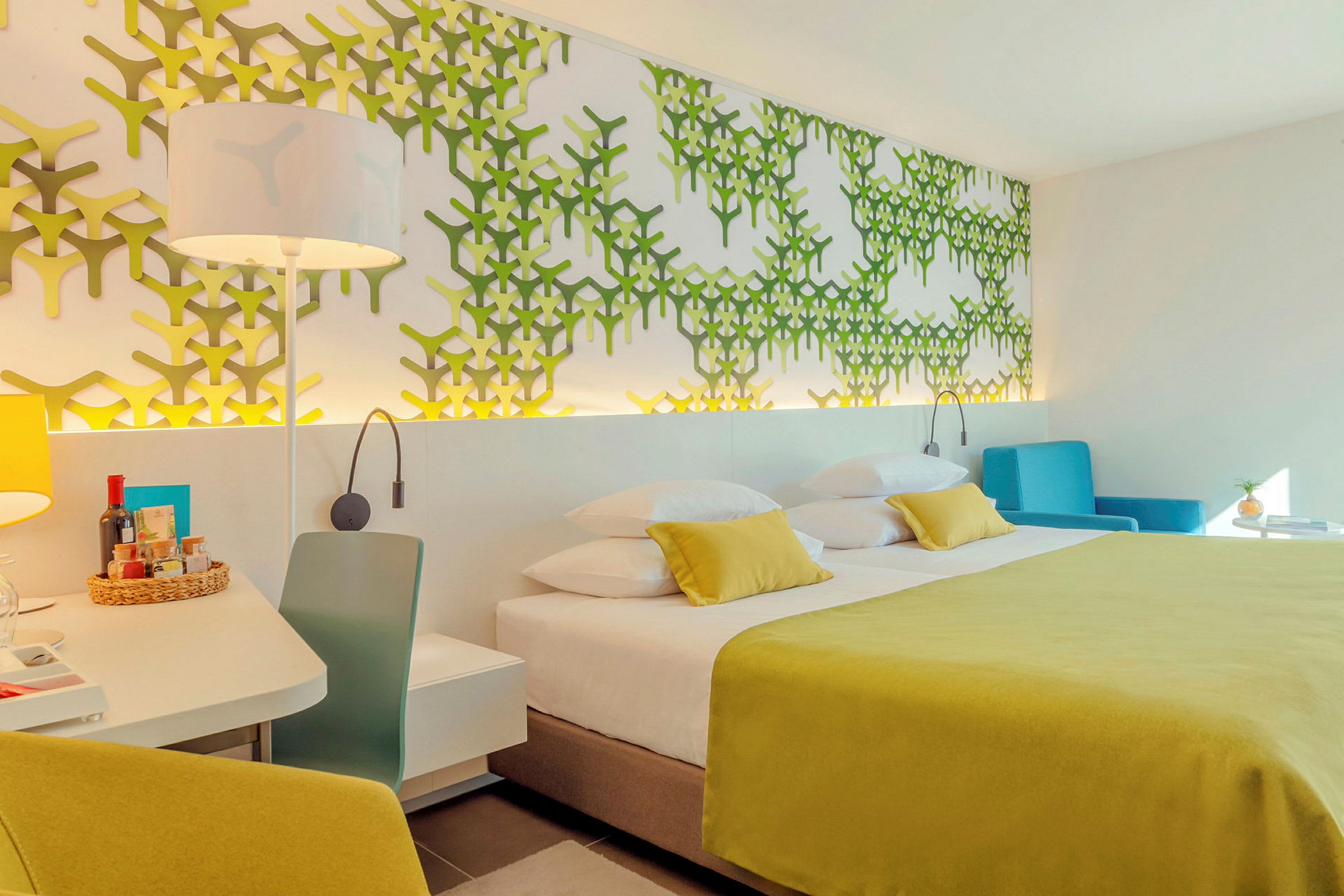 Ett hotelrum med en dubbelsäng, grön väggdekoration och en blå fåtölj. (AI-genererad text)