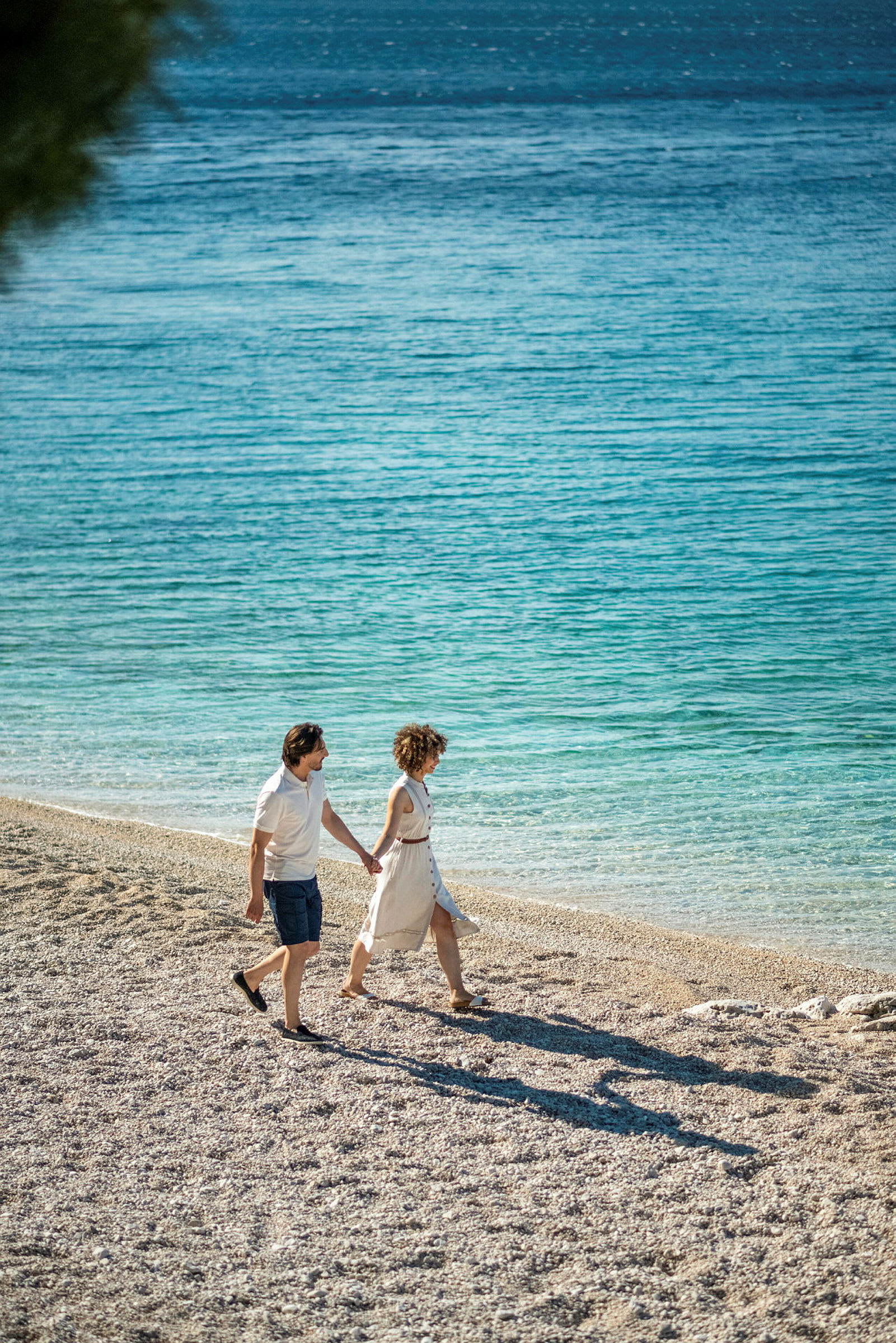 Två personer promenerar på en stenstrand vid havet. (AI-genererad text)