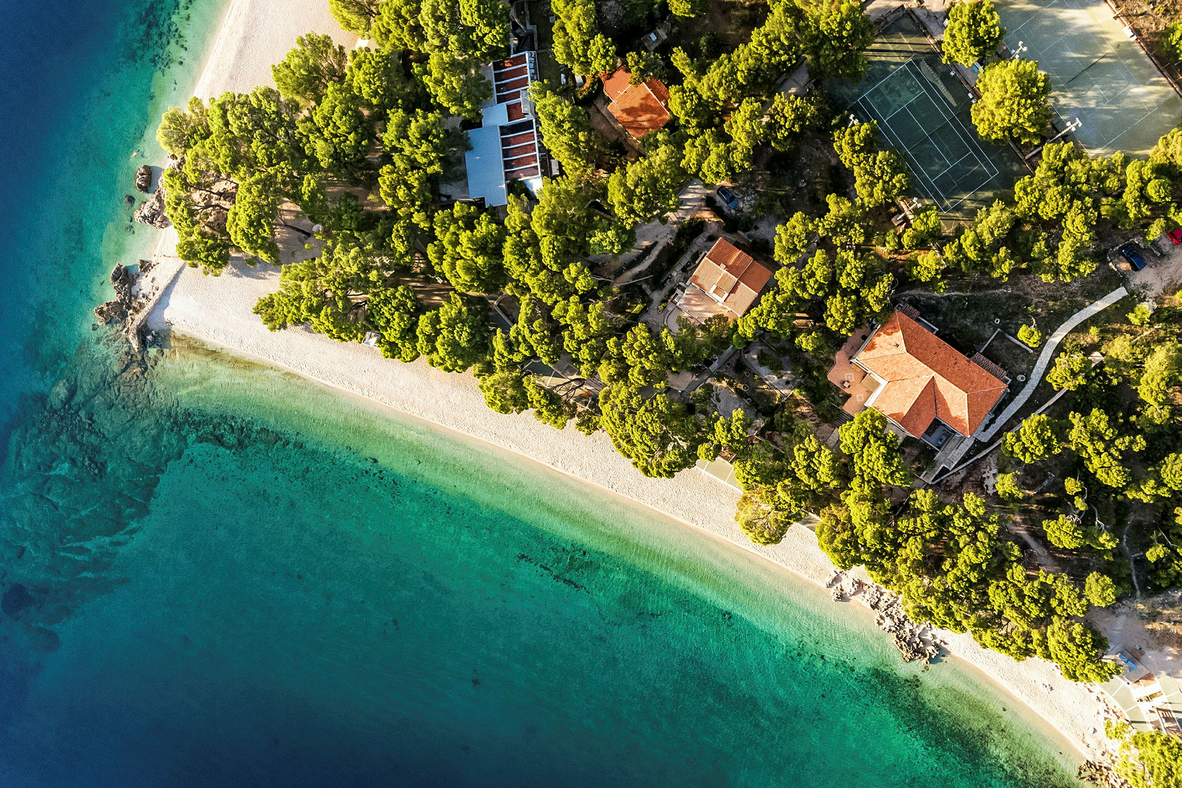 Flygfoto över en strand kantad av gröna träd och byggnader. (AI-genererad text)