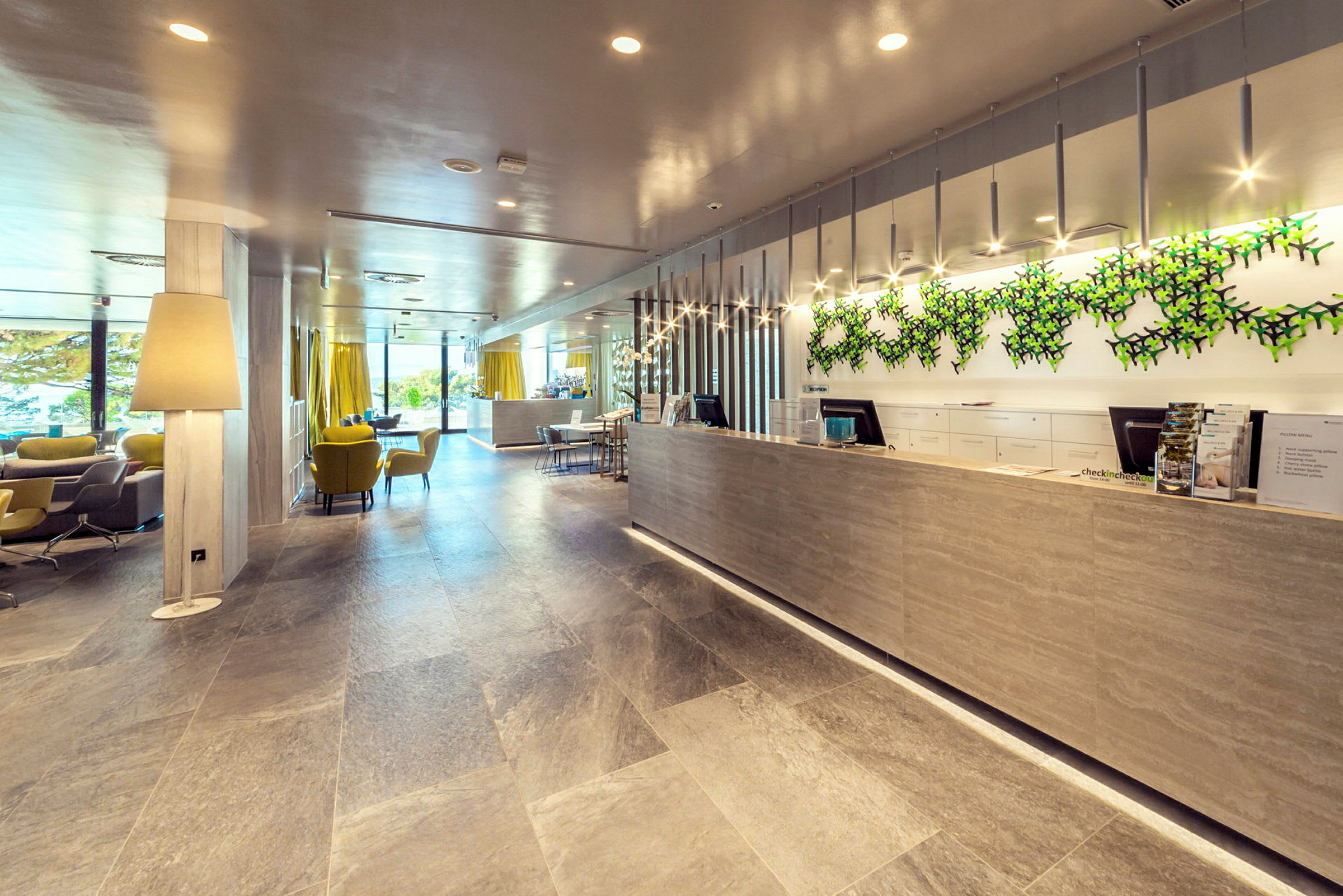 Receptionen i ett modernt hotell, med sittplatser, stora fönster och en dekorerad vägg. (AI-genererad text)