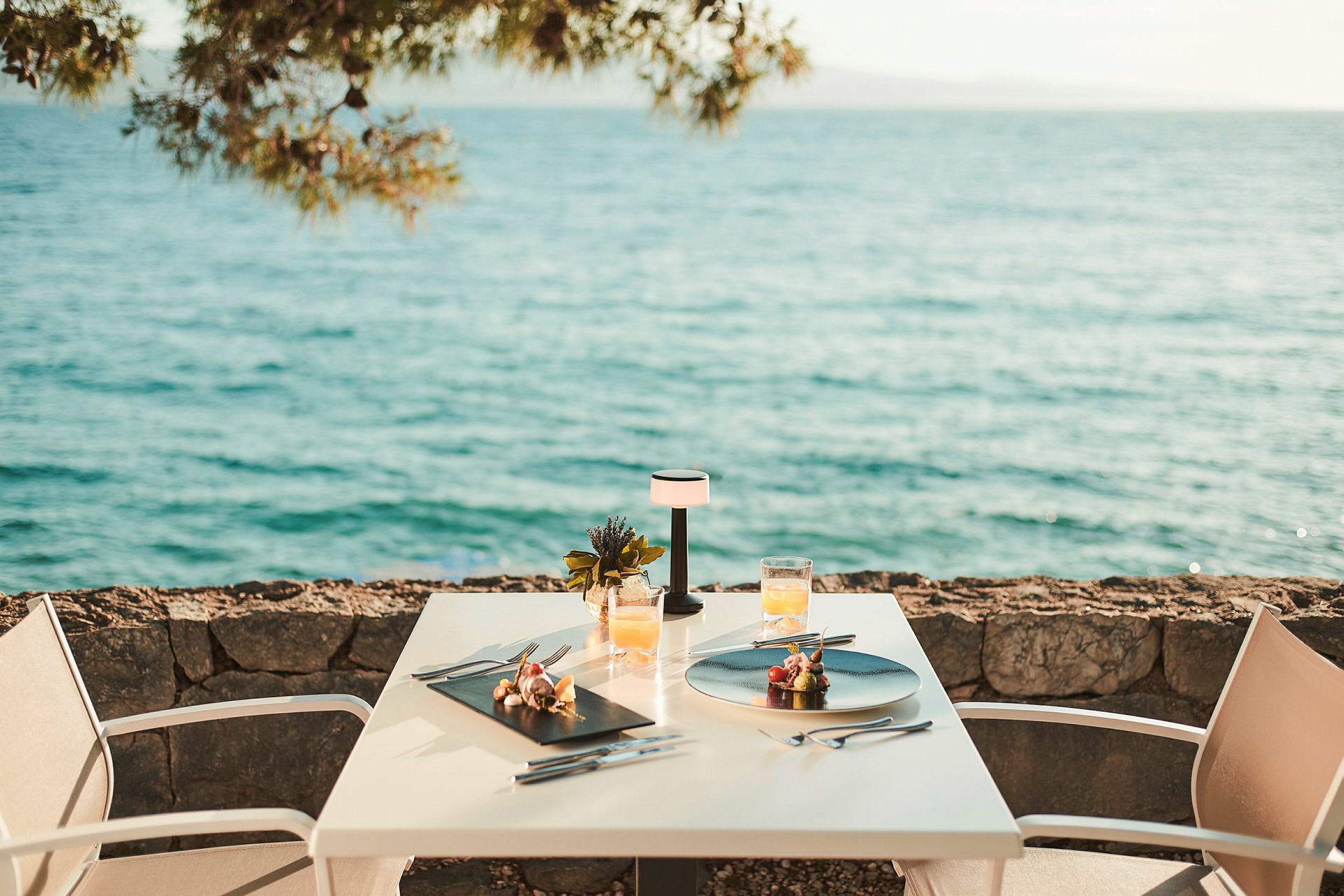 Två serverade tallrikar och dryck på ett bord vid havet. (AI-genererad text)