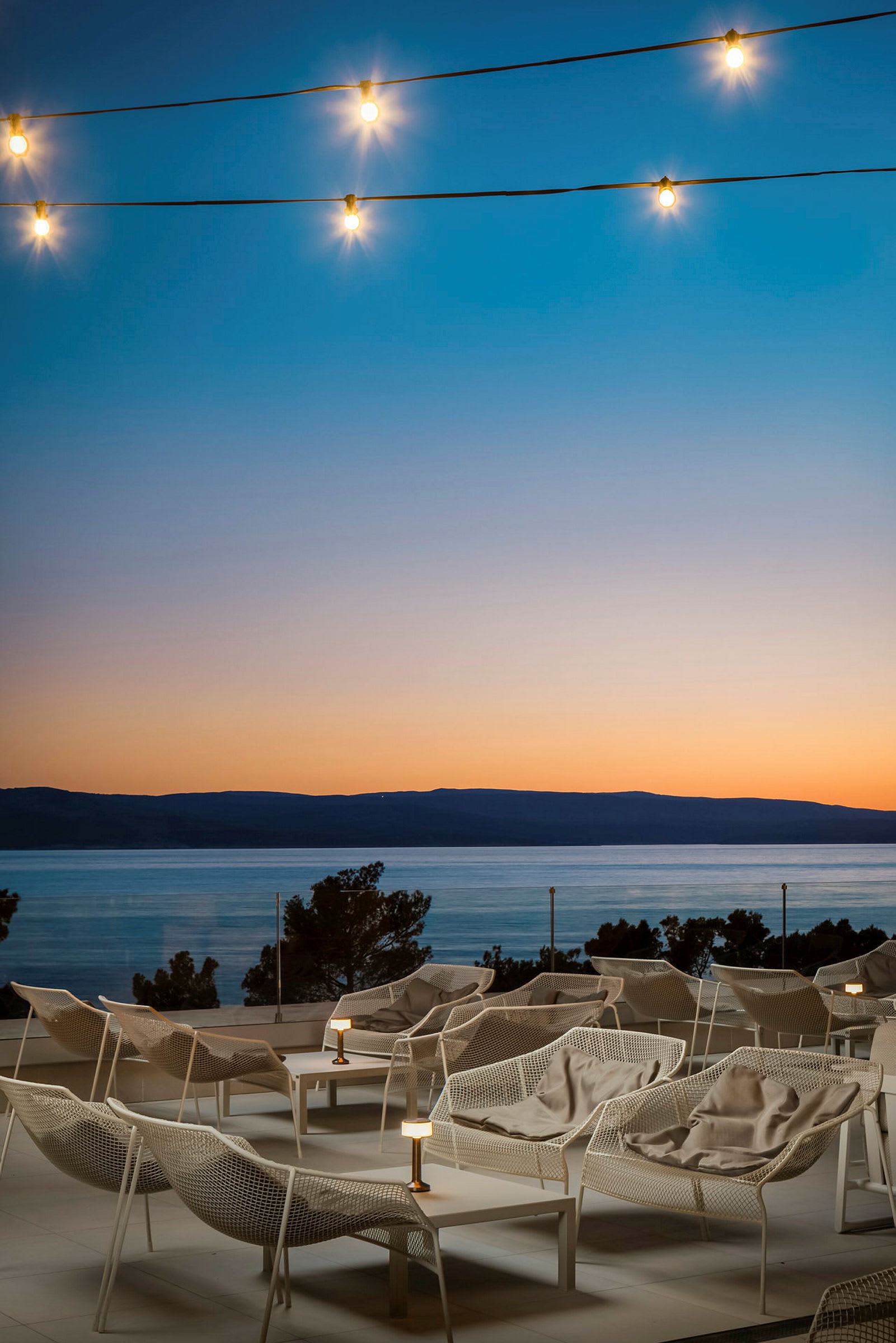 Vit loungestolar på en terrass med utsikt över havet under solnedgången, ljus för dekoration. (AI-genererad text)