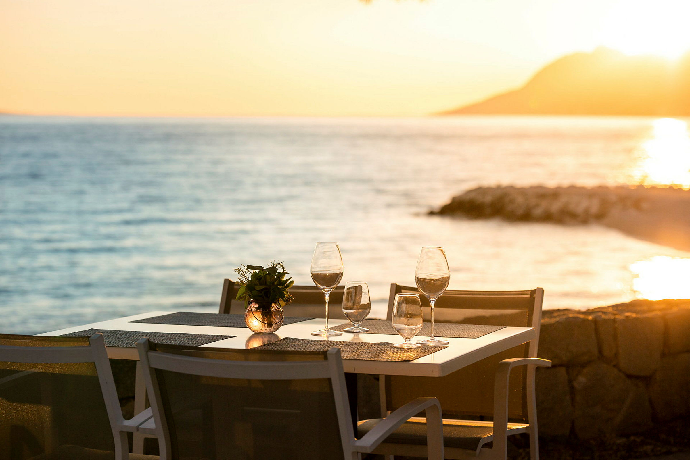 Ett dukat bord med glas och dekor vid havet i solnedgången. (AI-genererad text)