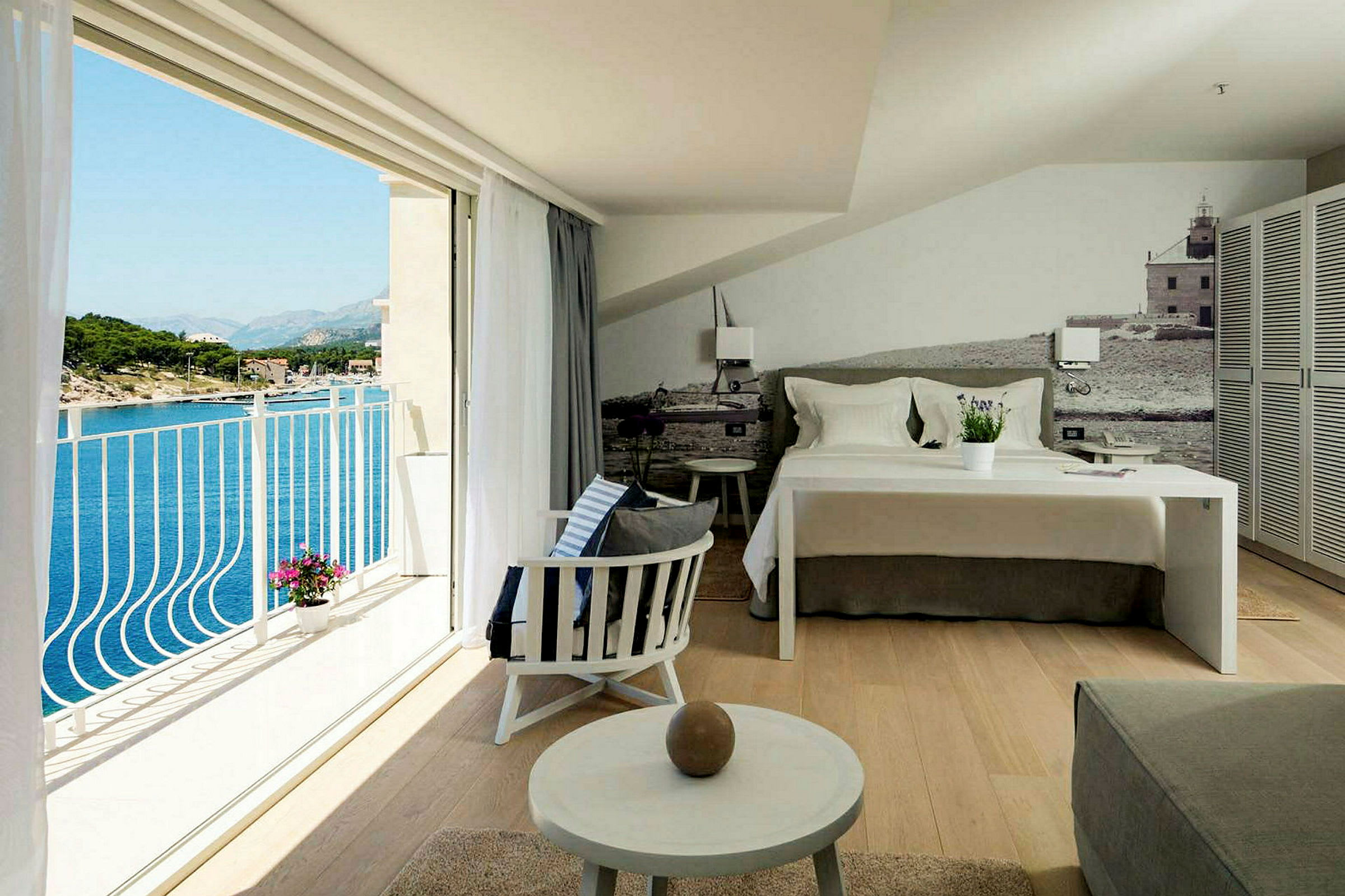 En hotellrum med en bäddad säng, sittområde och en balkong med utsikt över havet. (AI-genererad text)