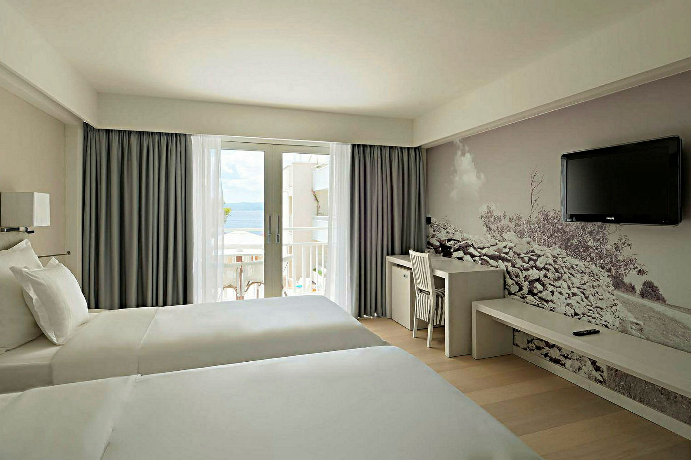 Hotellrum med två sängar, skrivbord och väggmålning samt utgång till balkong. (AI-genererad text)