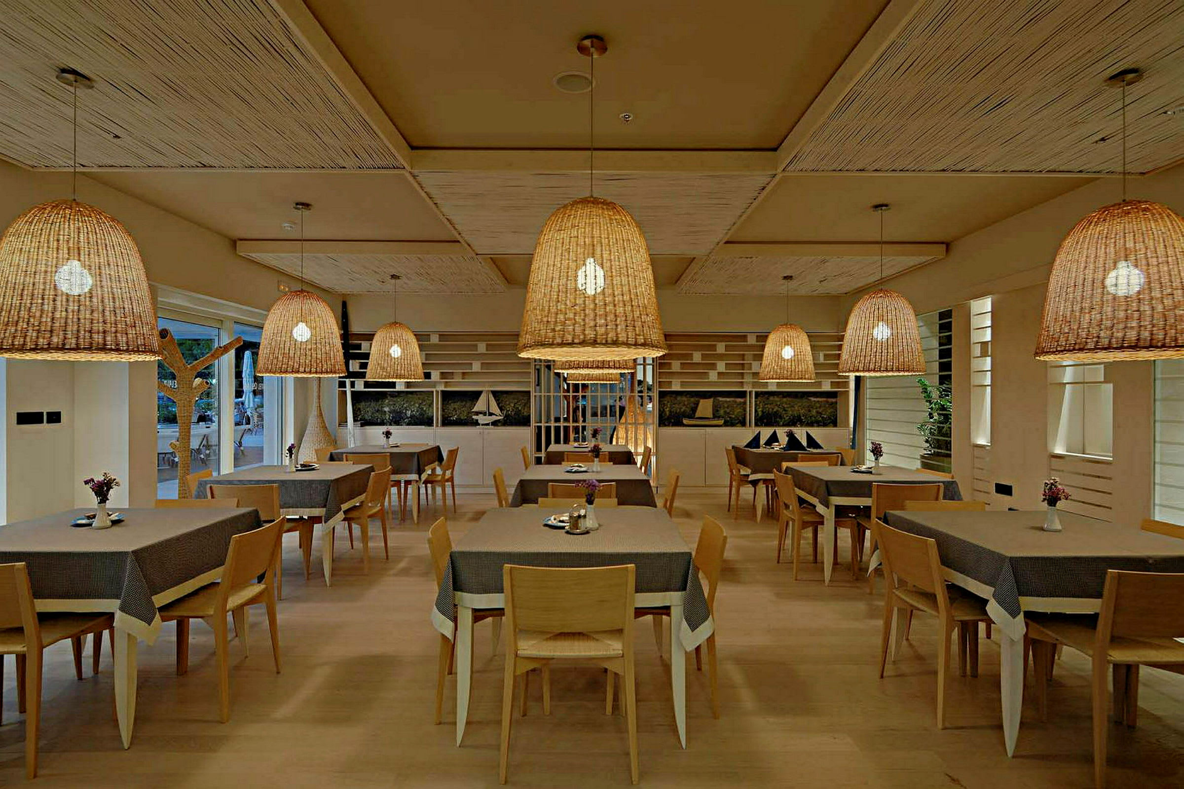 En restaurang med flera bord och stolar samt stora flätade taklampor. (AI-genererad text)
